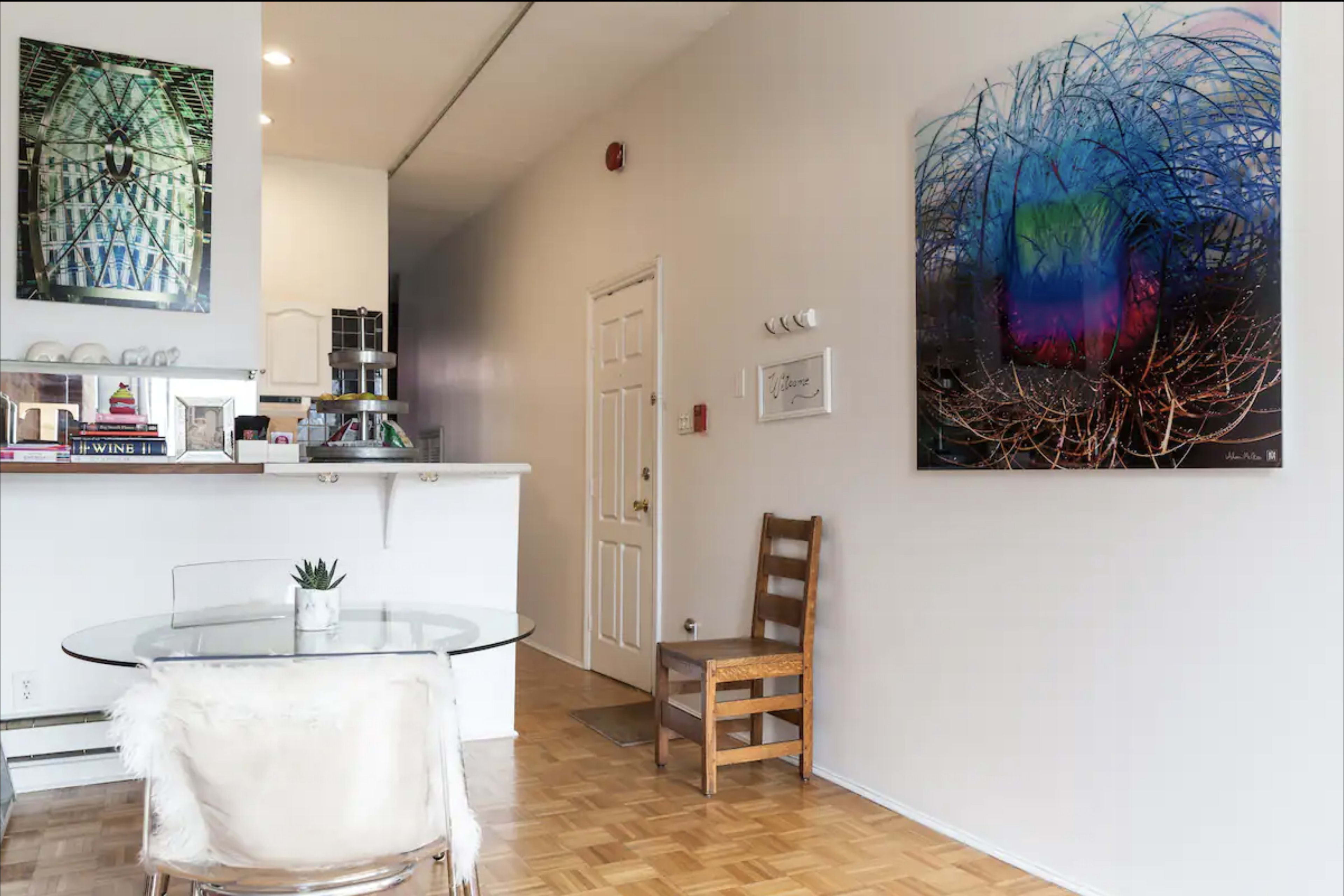 A modern living space features a circular glass dining table, a wooden chair, and a large abstract artwork on the wall.