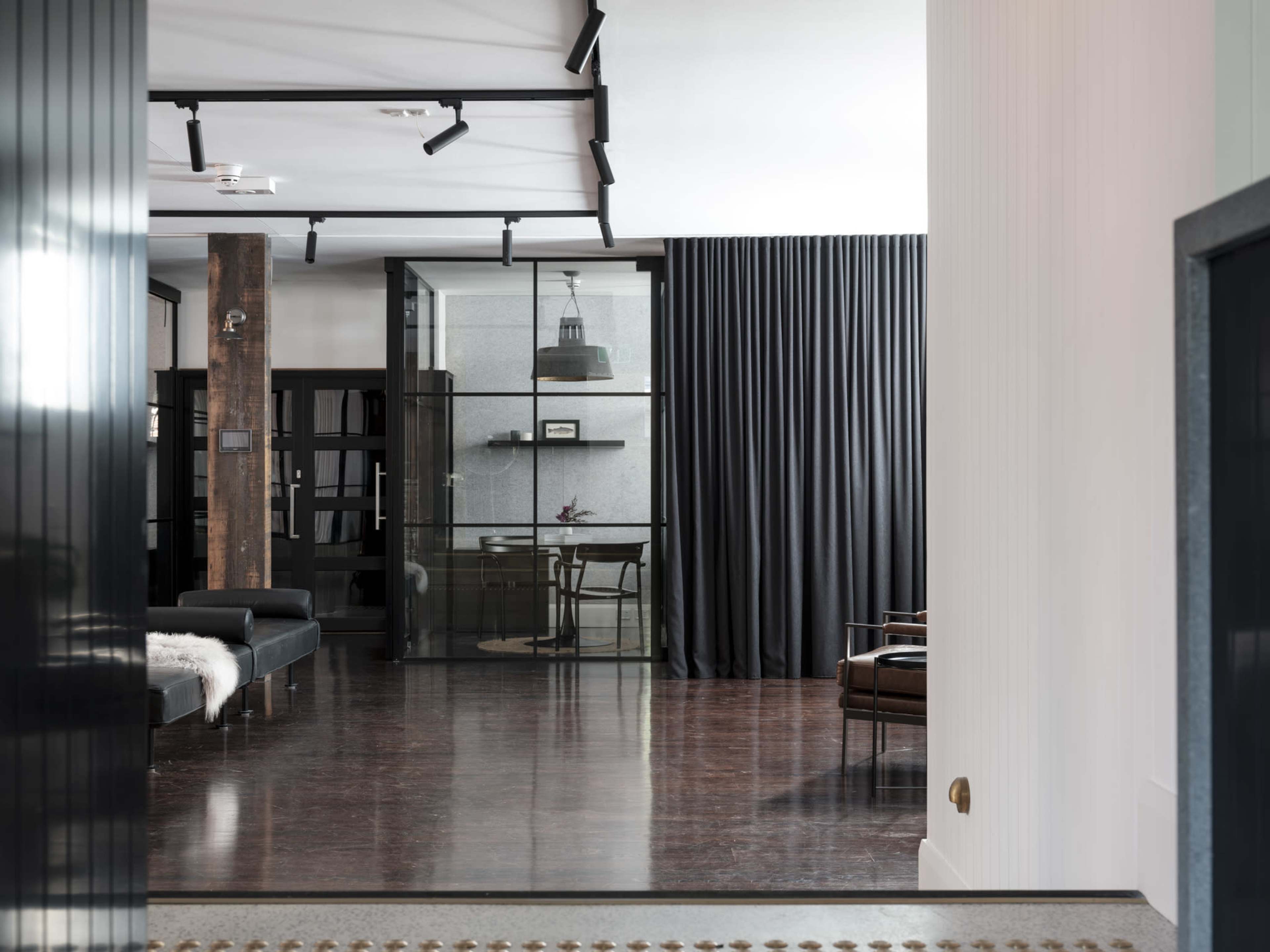 The image shows a modern interior space featuring a combination of sleek furniture, dark curtains, and a glass-walled meeting area.