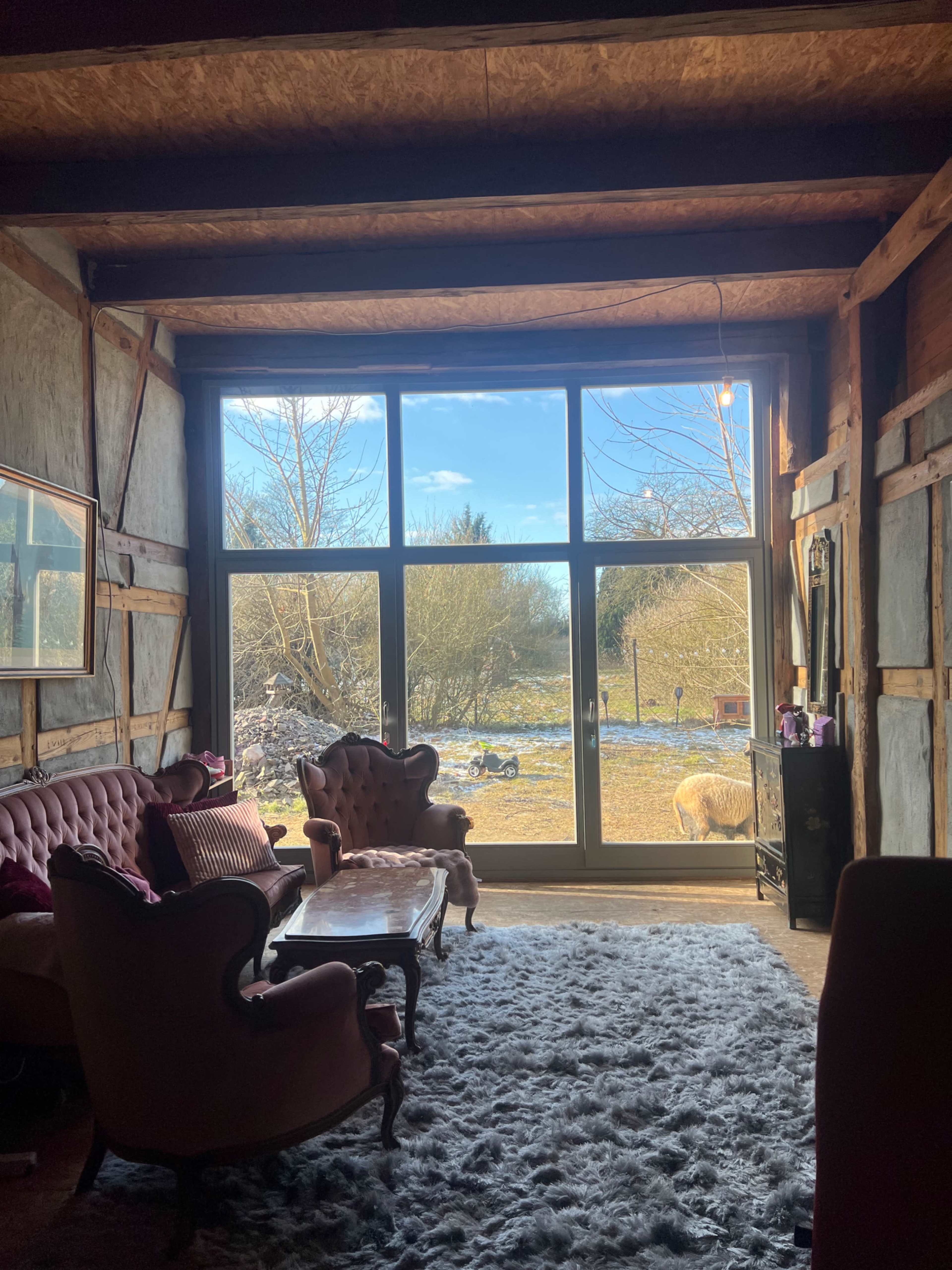 A cozy living room features a large window that opens to a view of a green yard with trees and a few animals in the distance.