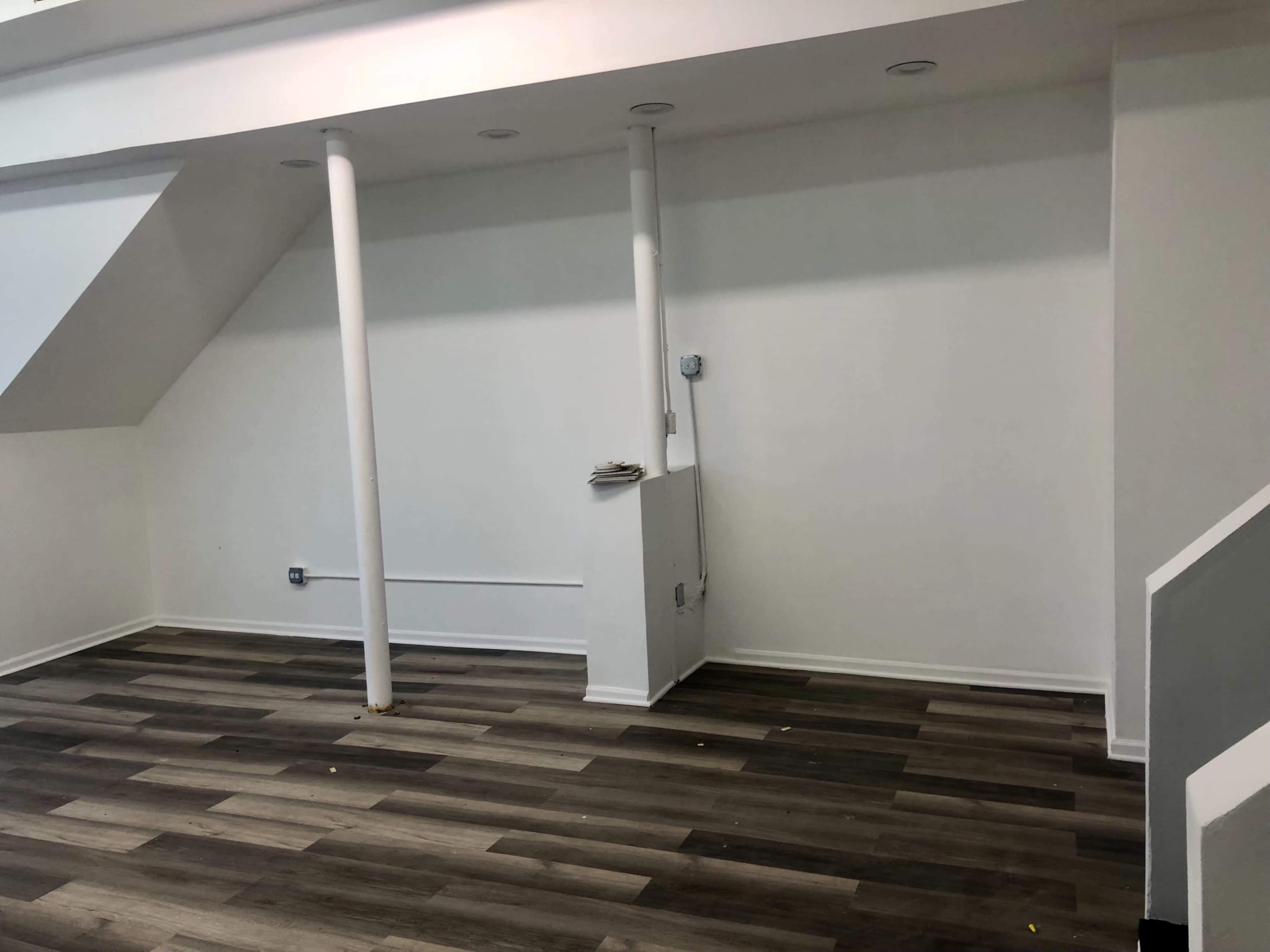 The image shows an empty room with wooden flooring and two white columns against a plain wall.