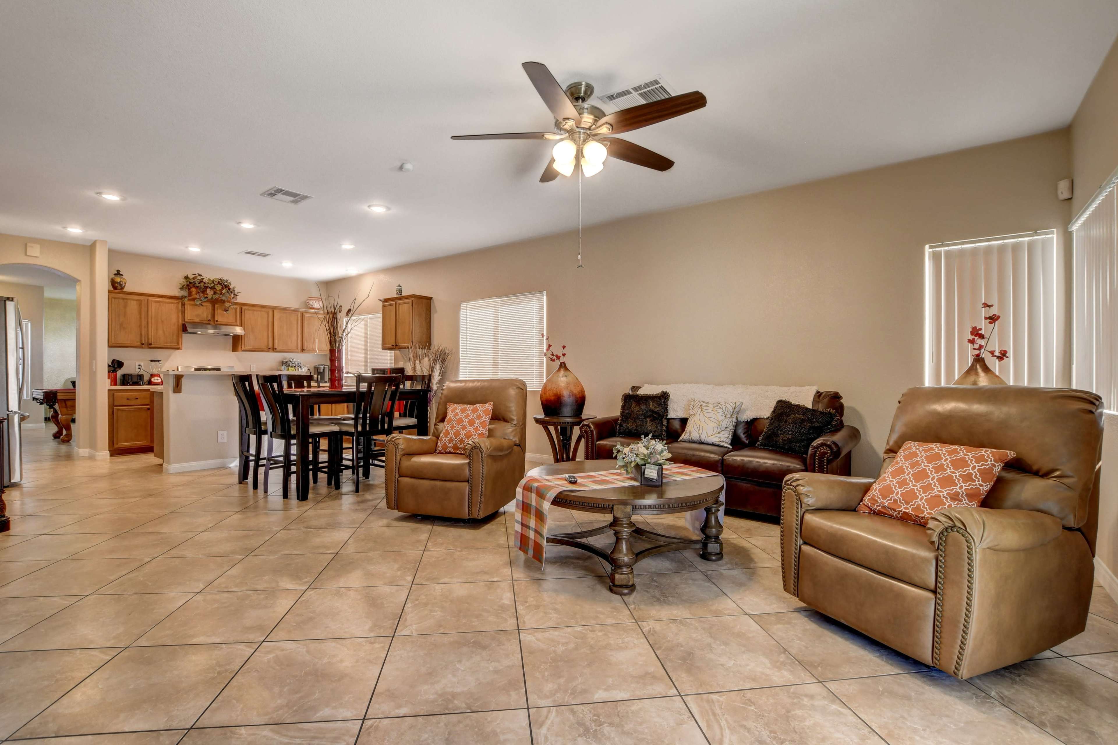 A spacious living room and dining area with two armchairs, a coffee table, and a kitchen visible in the background.
