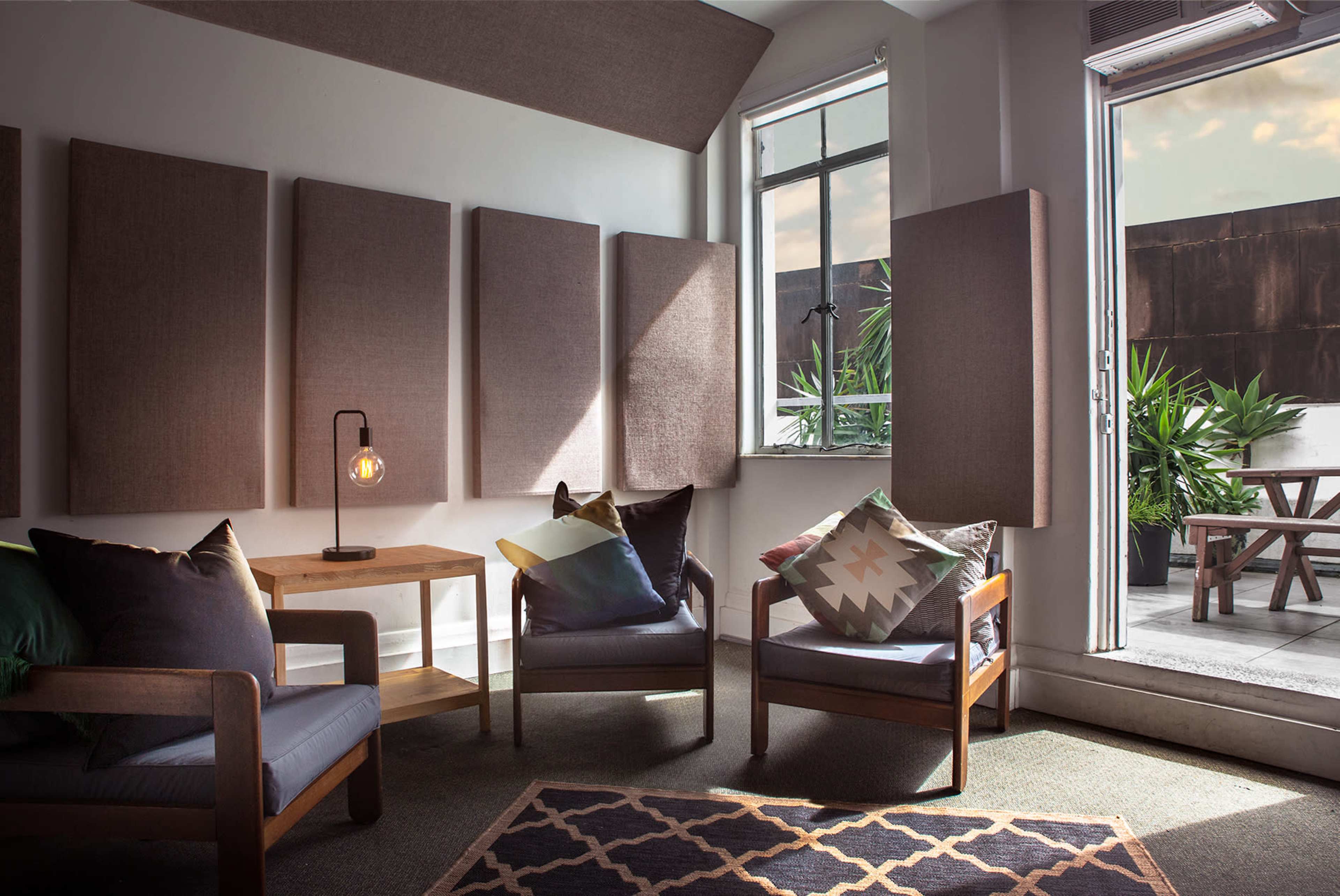 A cozy seating area with two chairs, a small wooden table, and textured wall panels, leading to an outdoor terrace with plants.