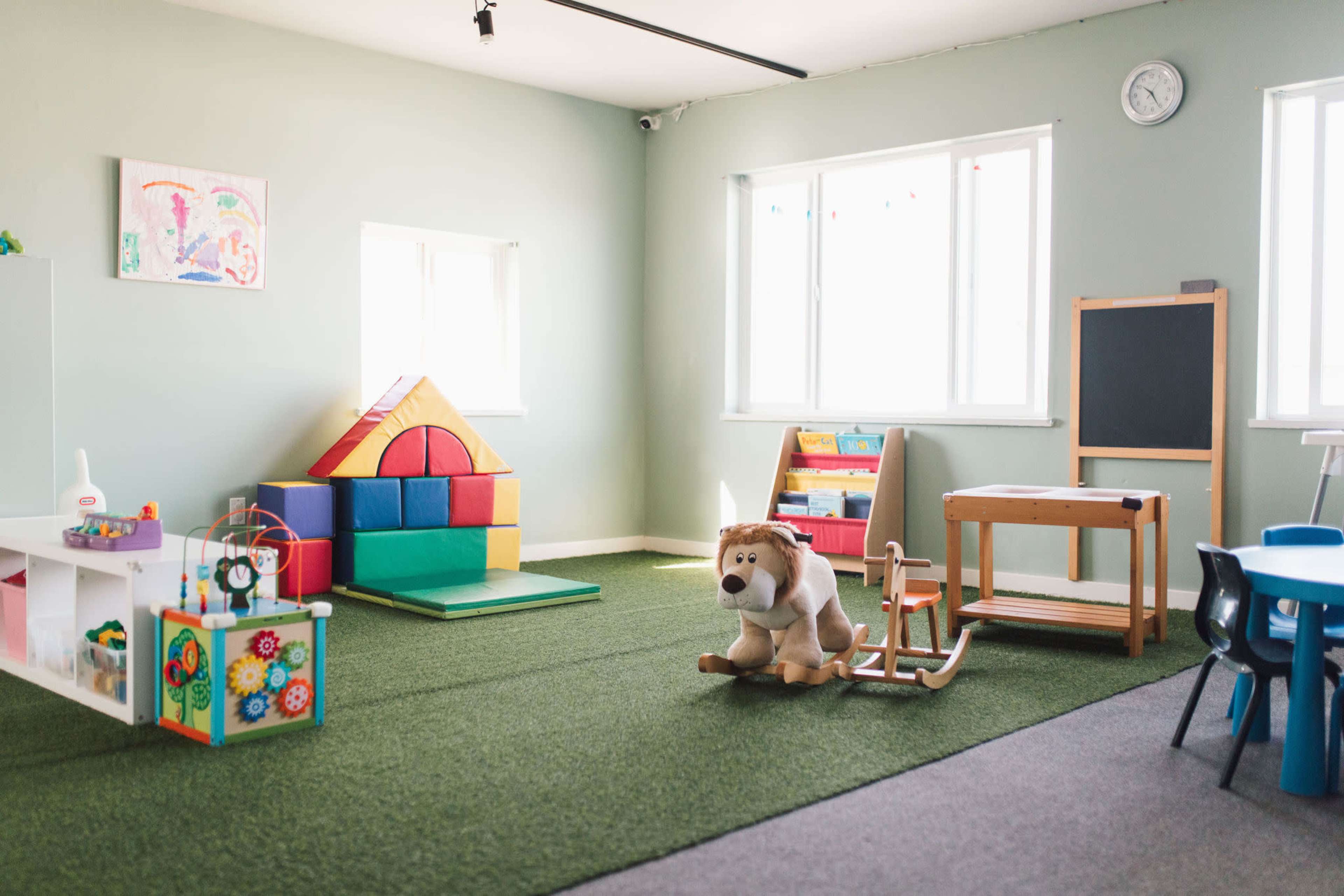 The image shows a bright, spacious playroom with colorful toys, a large plush dog, and a variety of play structures.