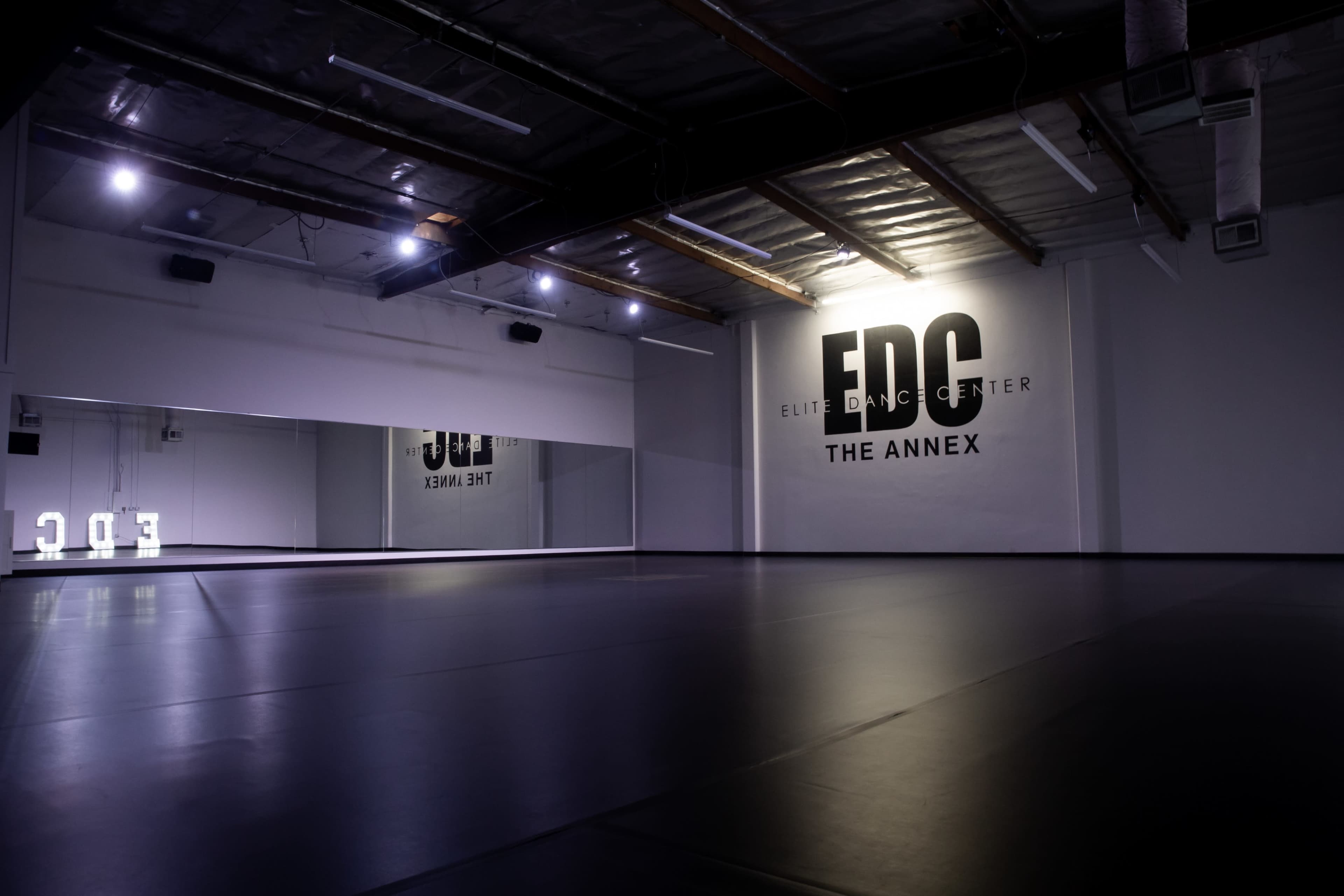 An empty dance studio features a mirrored wall and a large logo on the back wall.