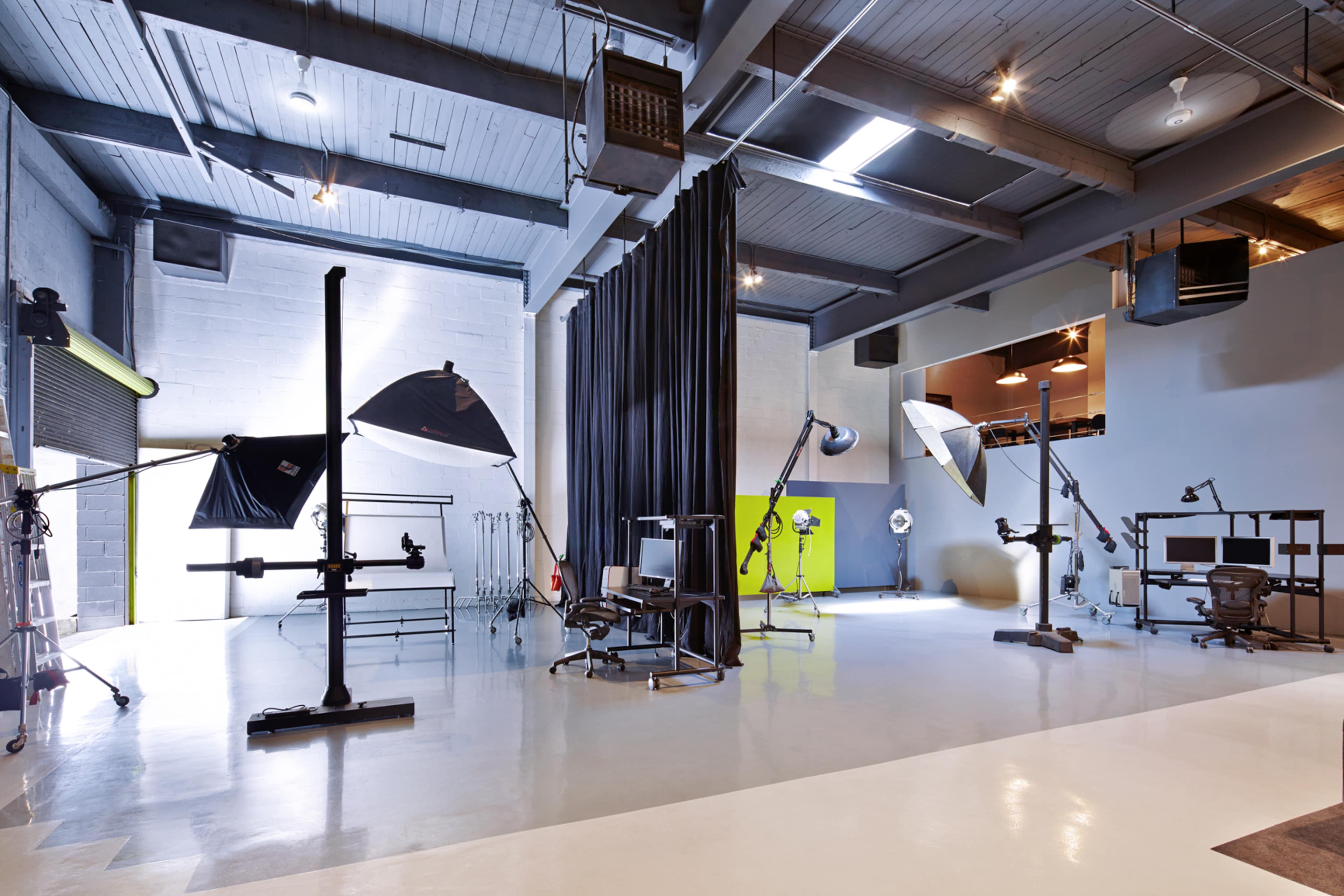 A spacious photography studio with various lighting setups, a chair, and a backdrop curtain.