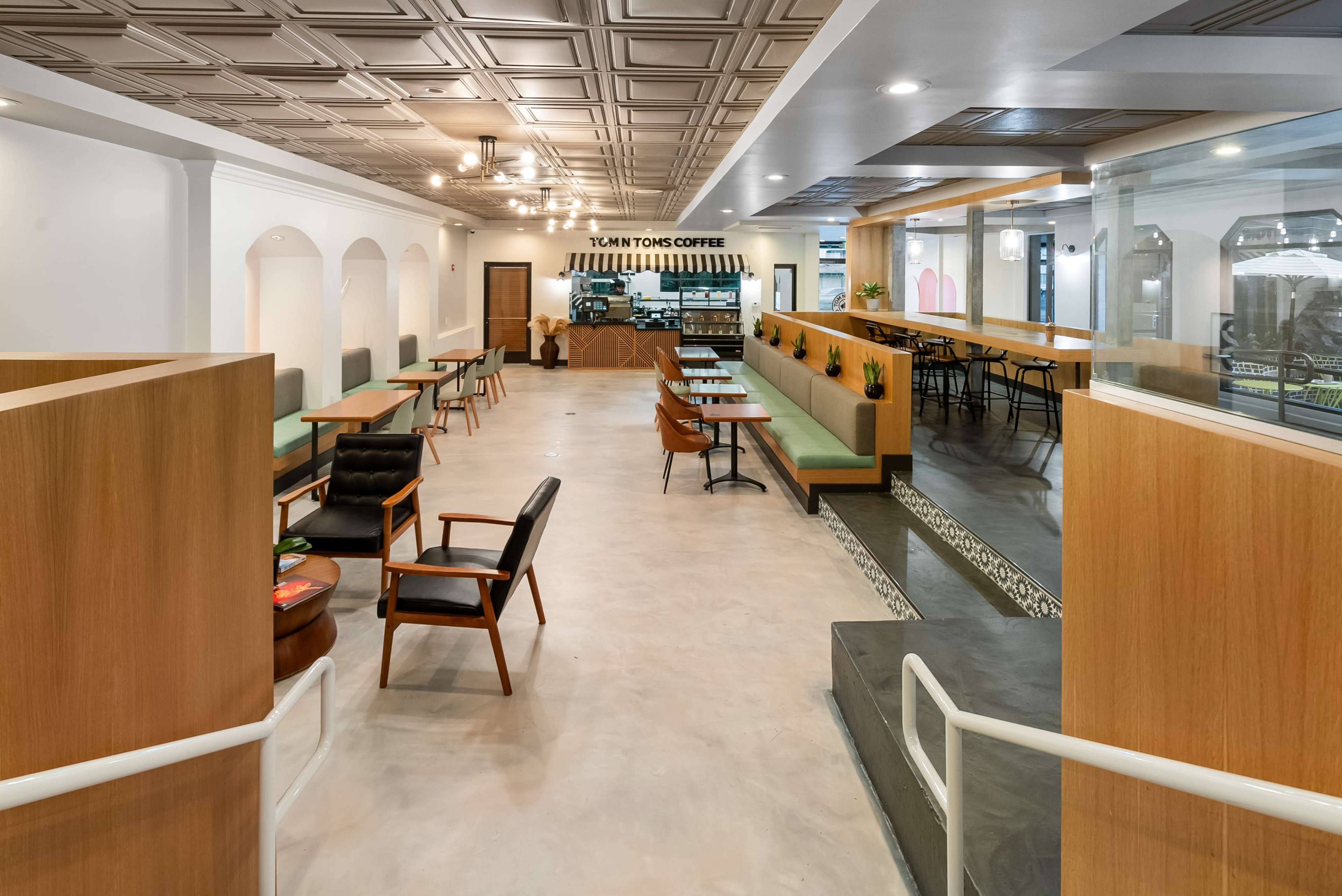 A modern coffee shop interior with wooden seating arrangements, tables, and a counter in the background.
