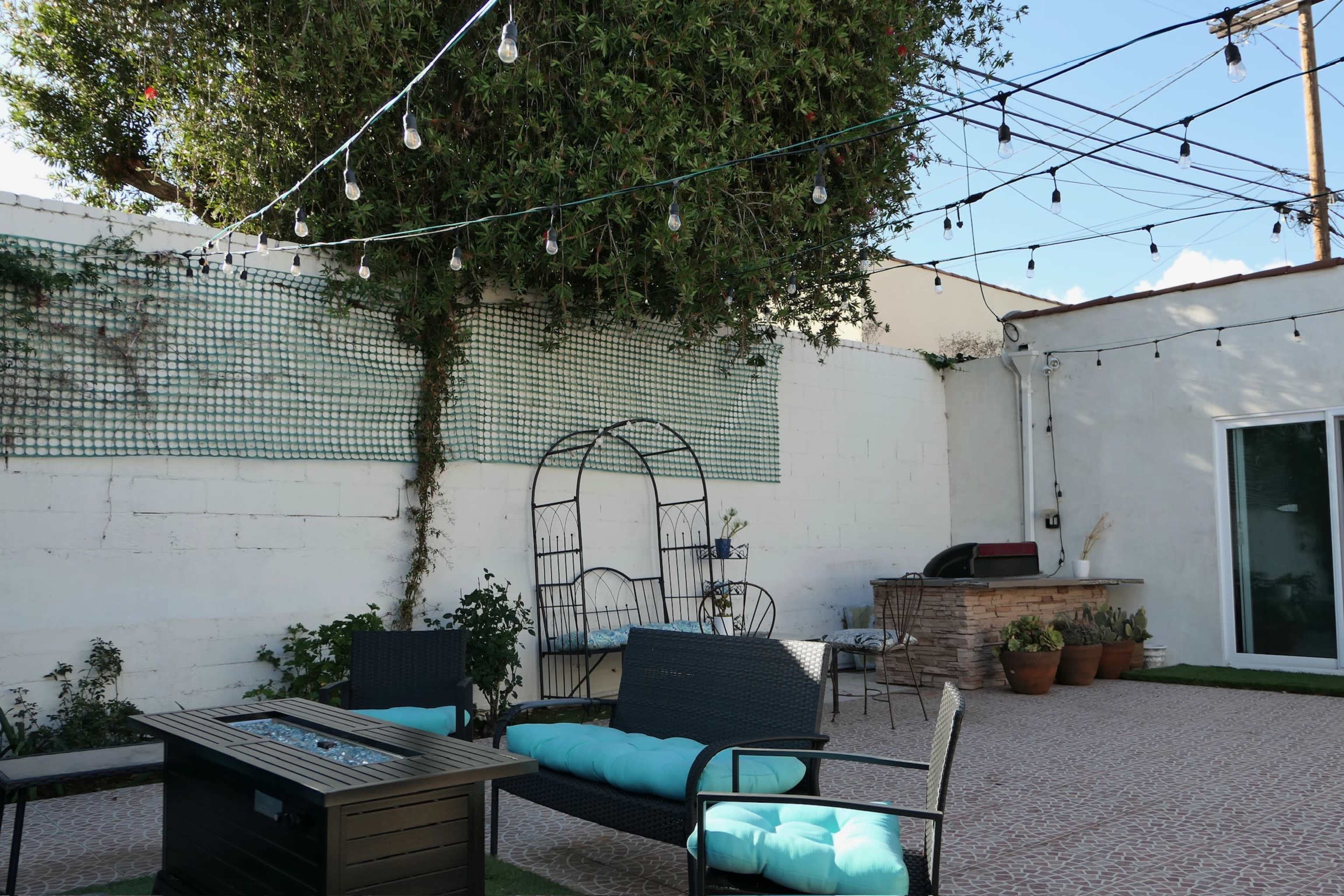 A patio area with a fire pit, seating furniture, a stone barbecue, and string lights suspended overhead.