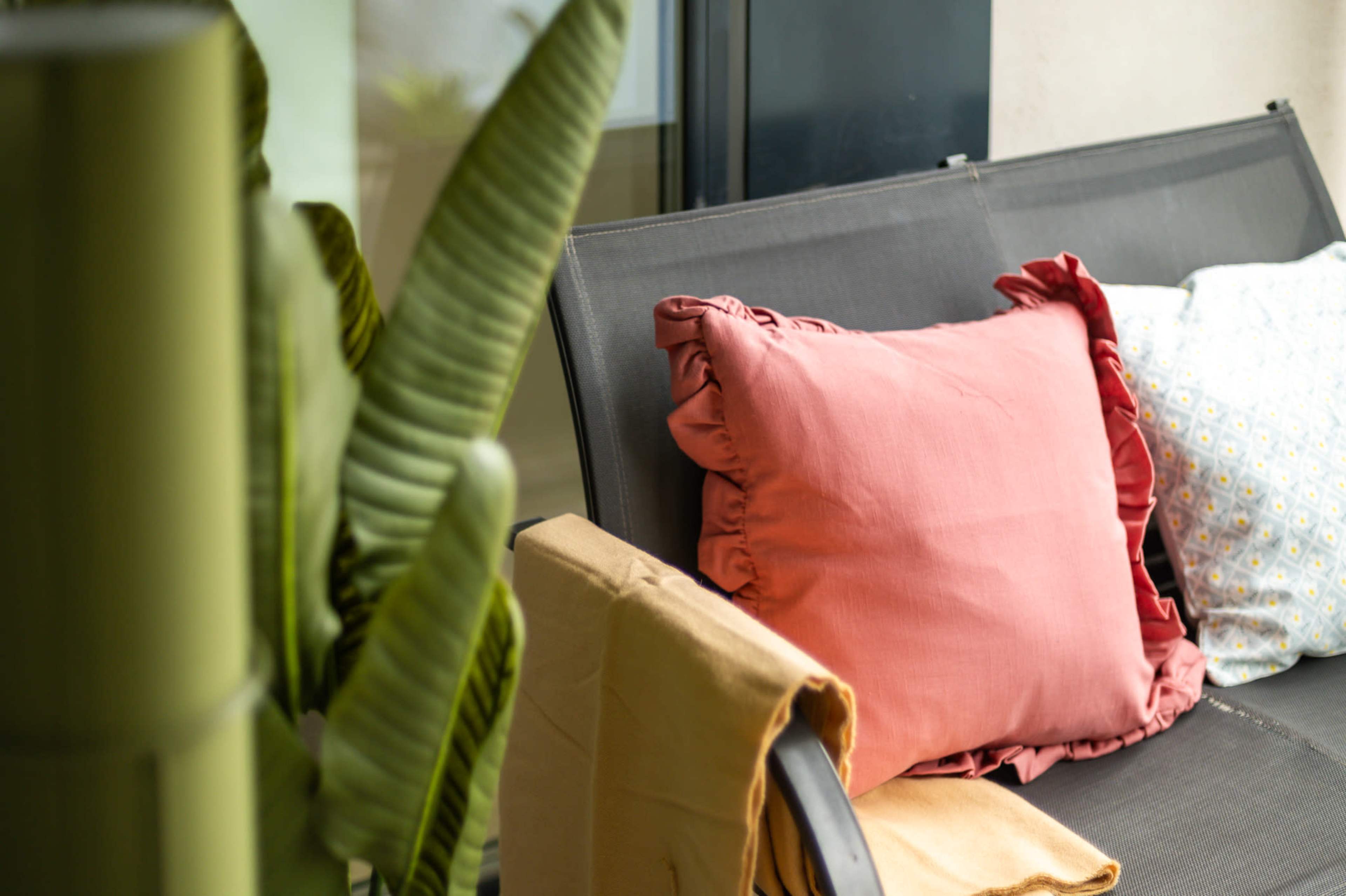 A gray chair with decorative pillows and a throw blanket is positioned beside a large green plant.