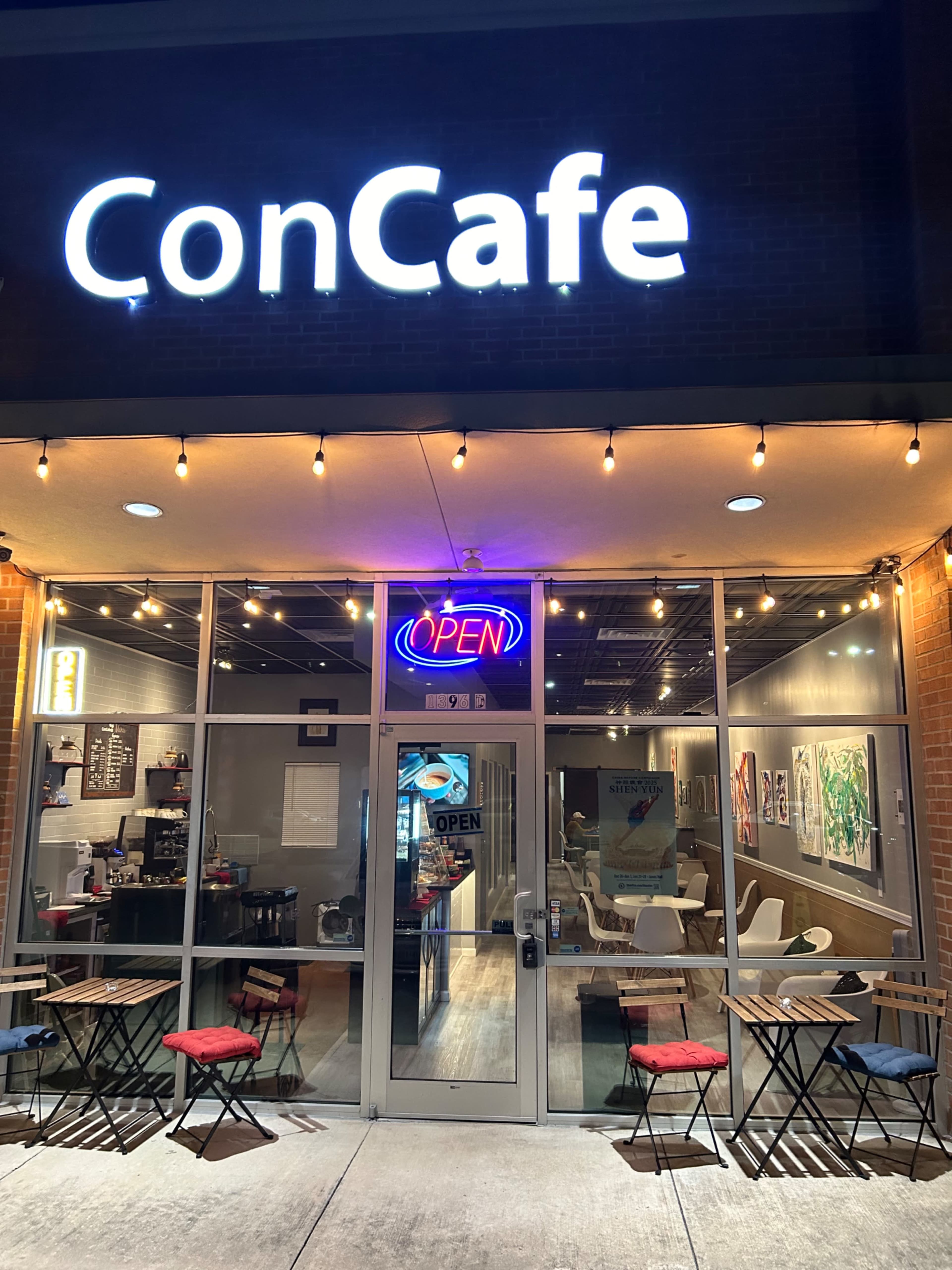 The image shows a café entrance with a brightly lit "ConCafe" sign and an open neon sign, featuring tables and chairs outside.