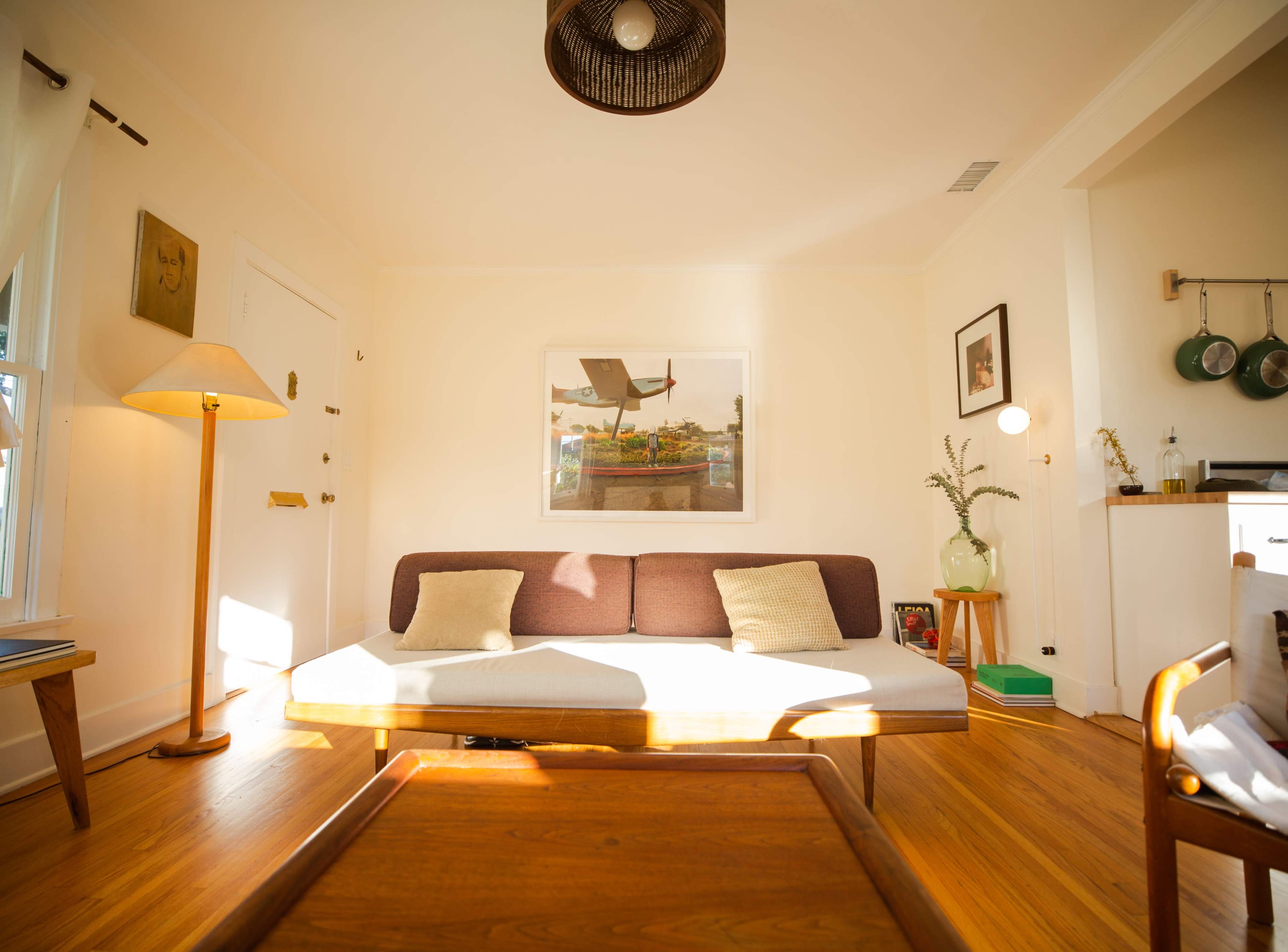 The image shows a cozy living room with a minimalist sofa, a wooden coffee table, and natural light streaming through the windows.