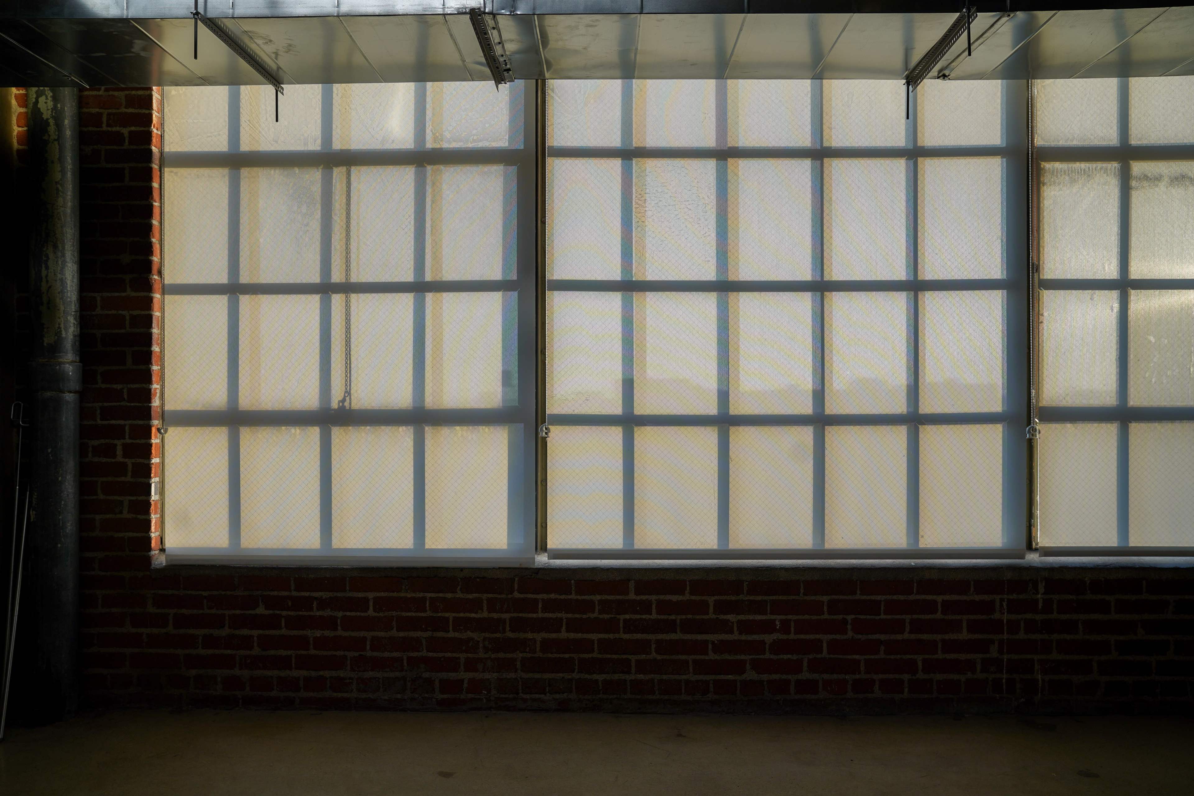 The image shows a section of a wall with a series of large, grid-patterned translucent windows above a red brick surface.