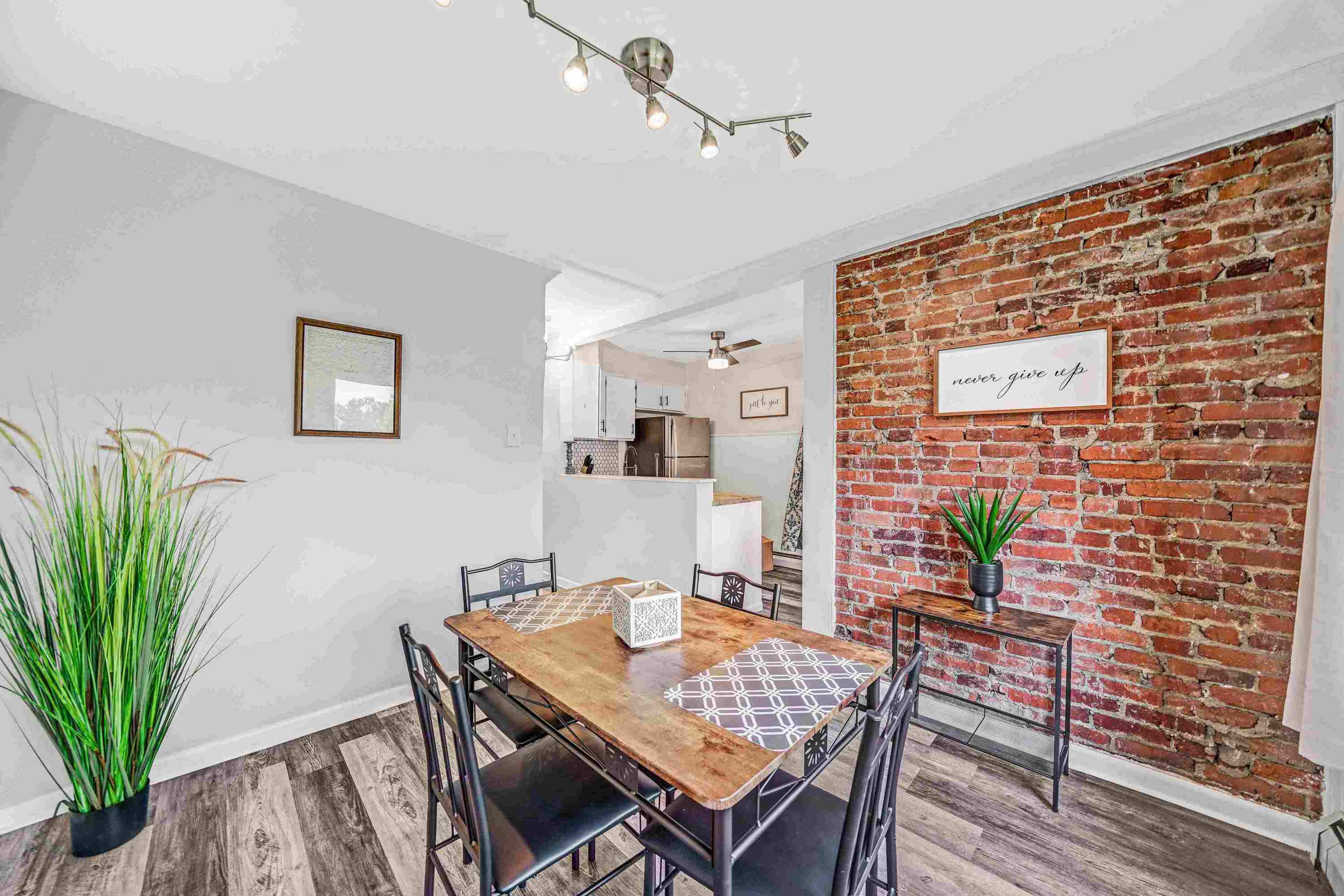 A dining area with a wooden table surrounded by black chairs, a brick accent wall, and decorative plants.