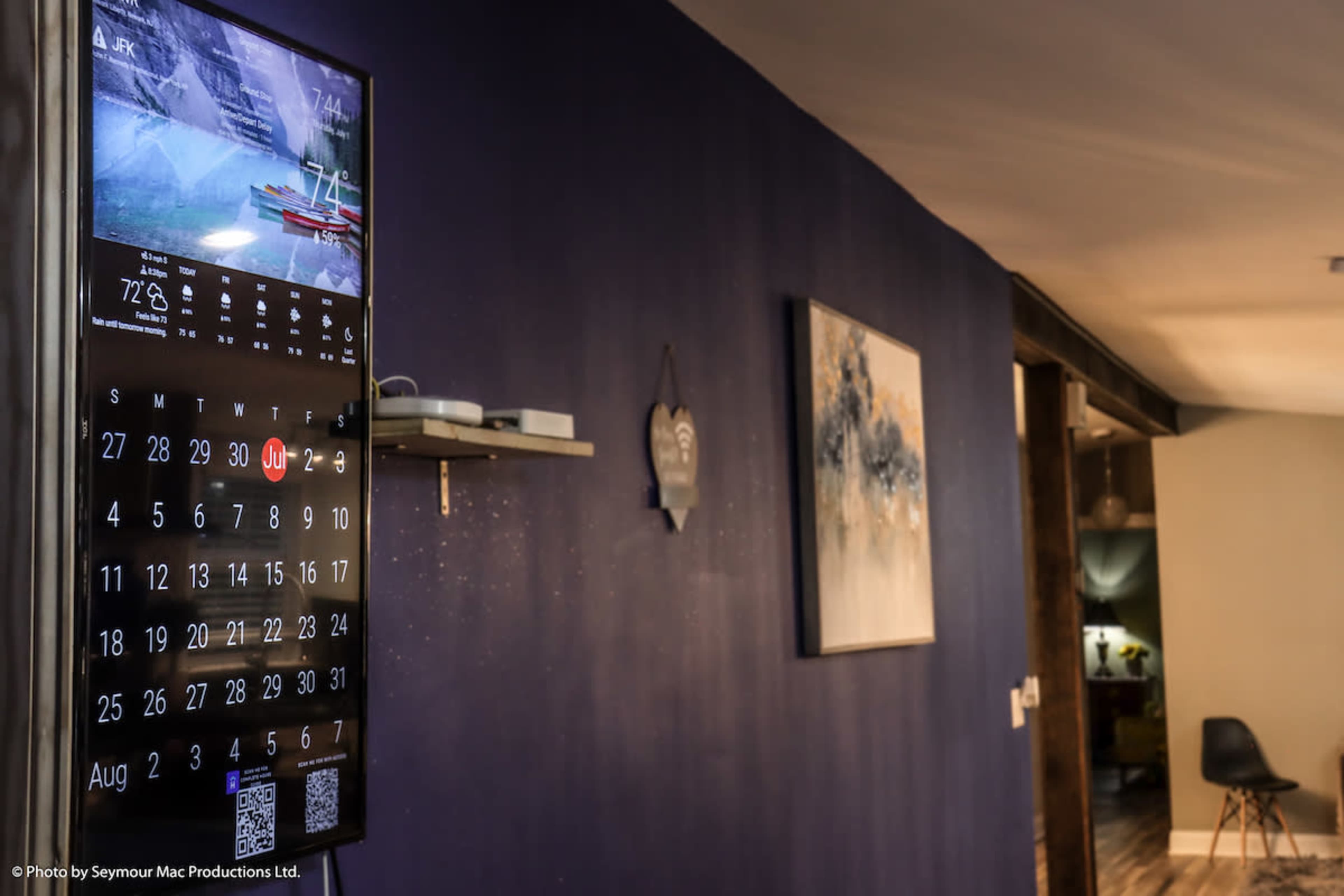 A wall-mounted digital display shows the date and temperature in a modern interior space with dark blue walls and a contrasting light fixture.