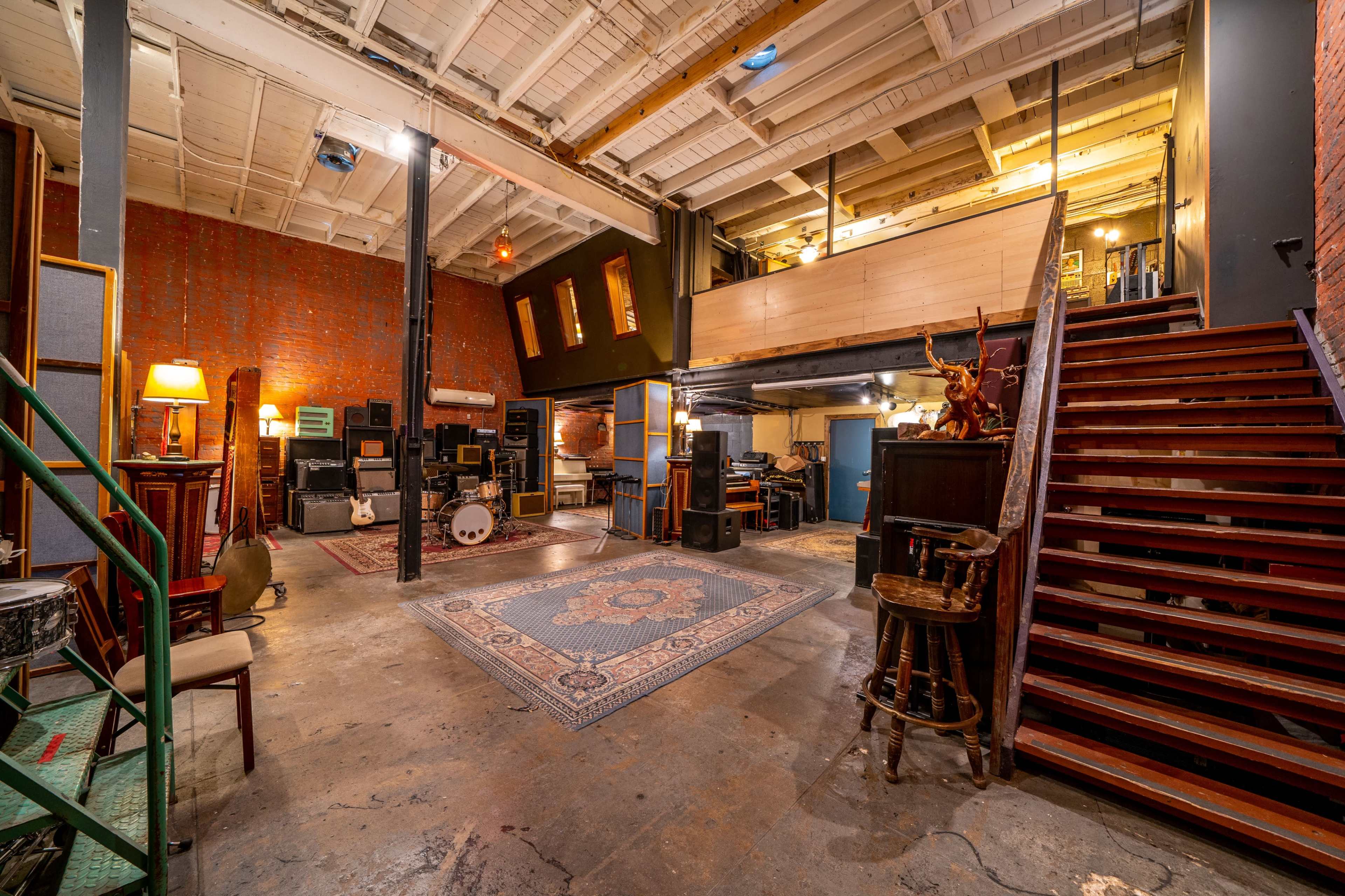 An interior space with a stage area, musical equipment, a carpet on the floor, and a staircase leading to a second level.