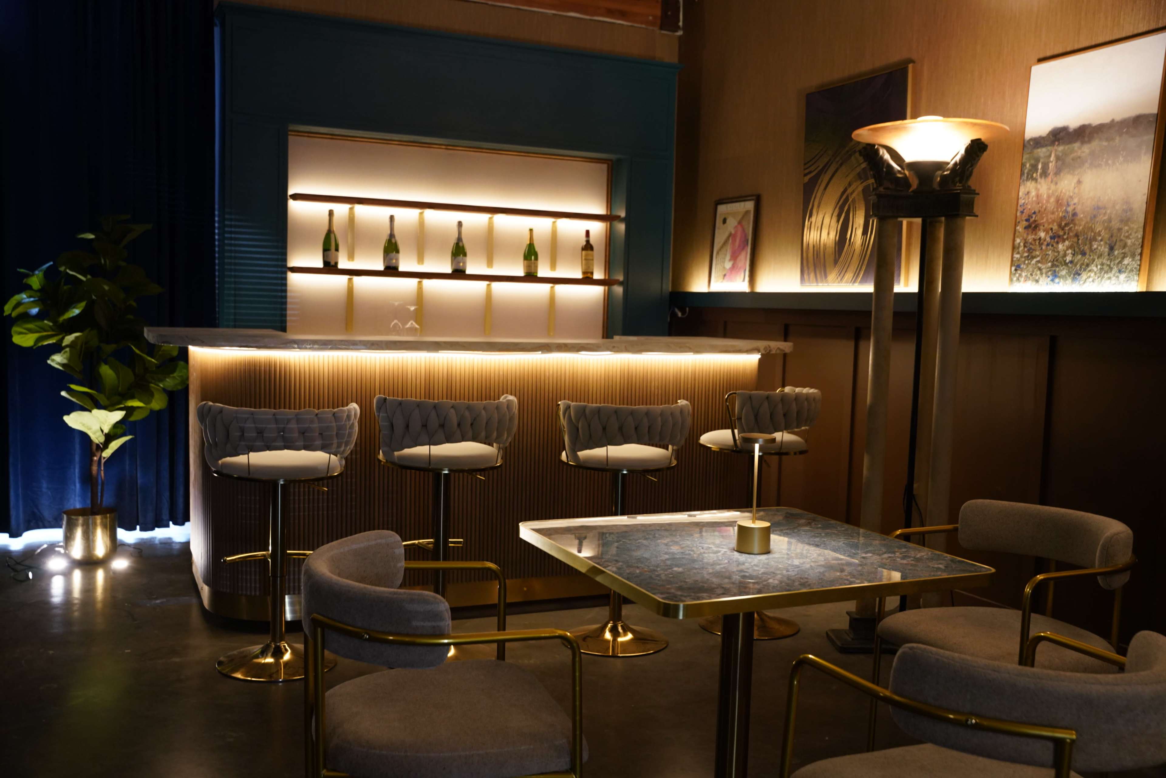 A modern bar area features a sleek countertop illuminated by warm lighting, complemented by stylish seating and decorative art on the walls.