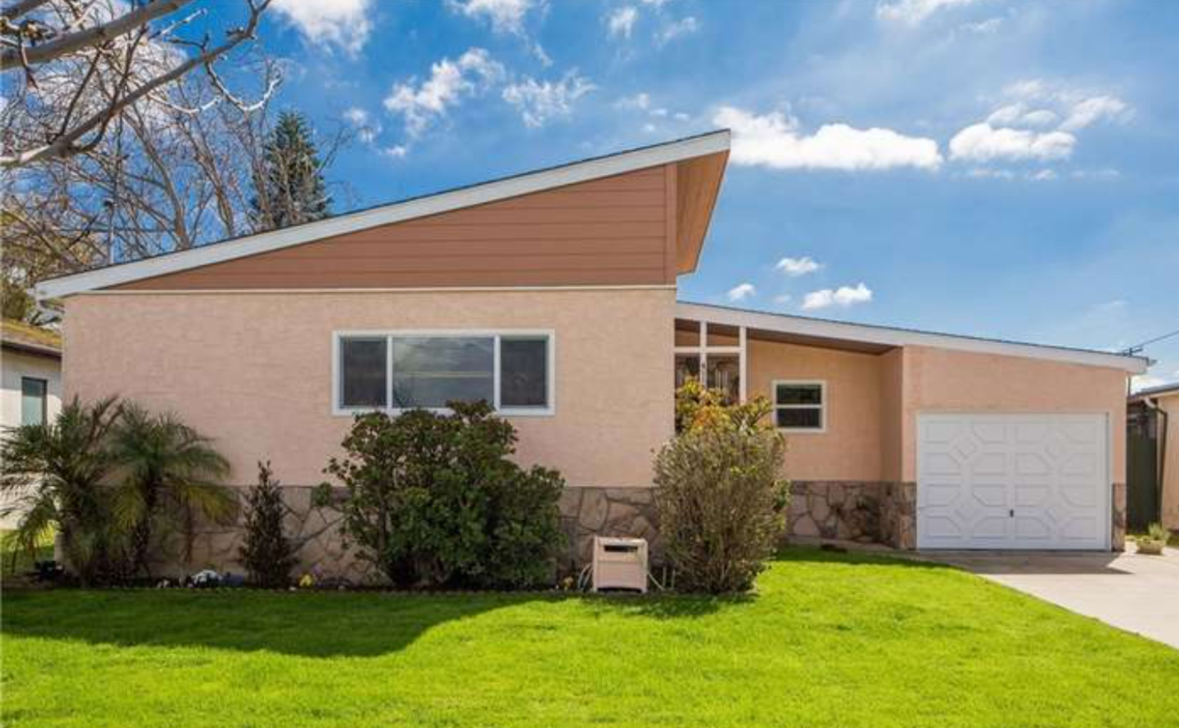 A single-story house with a sloped roof features a mix of light-colored stucco and stone, situated on a grassy lawn.