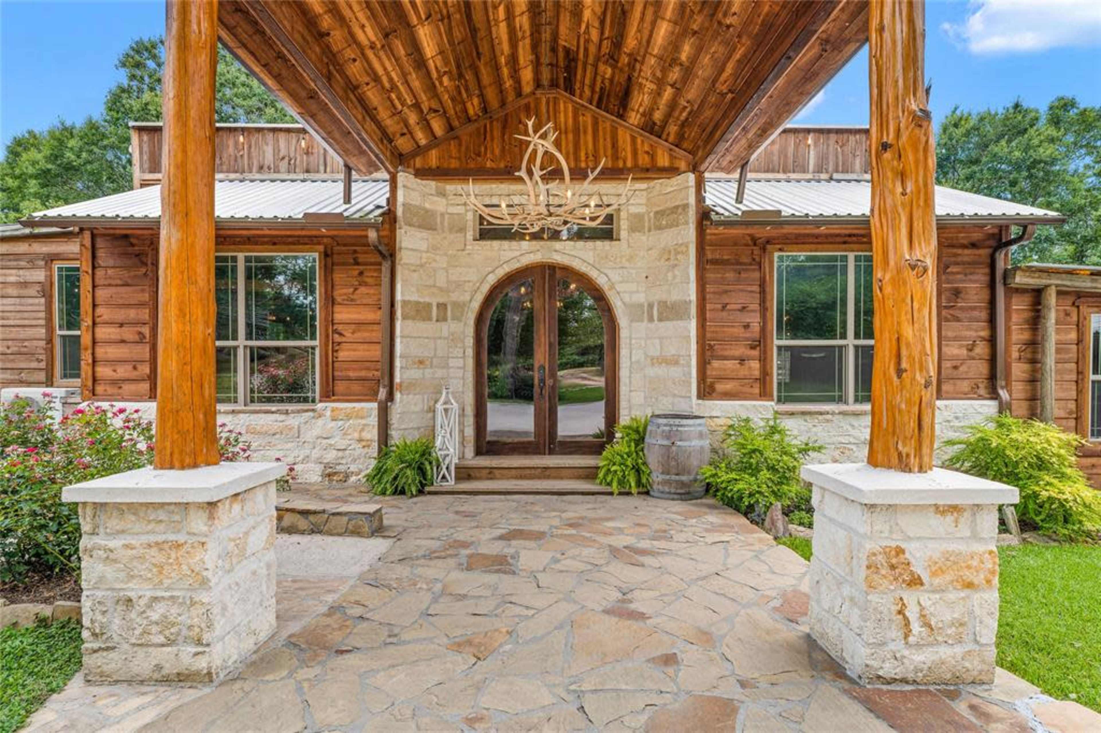 The entryway features a stone pathway leading to an arched wooden door, framed by columns and a covered porch with a chandelier.