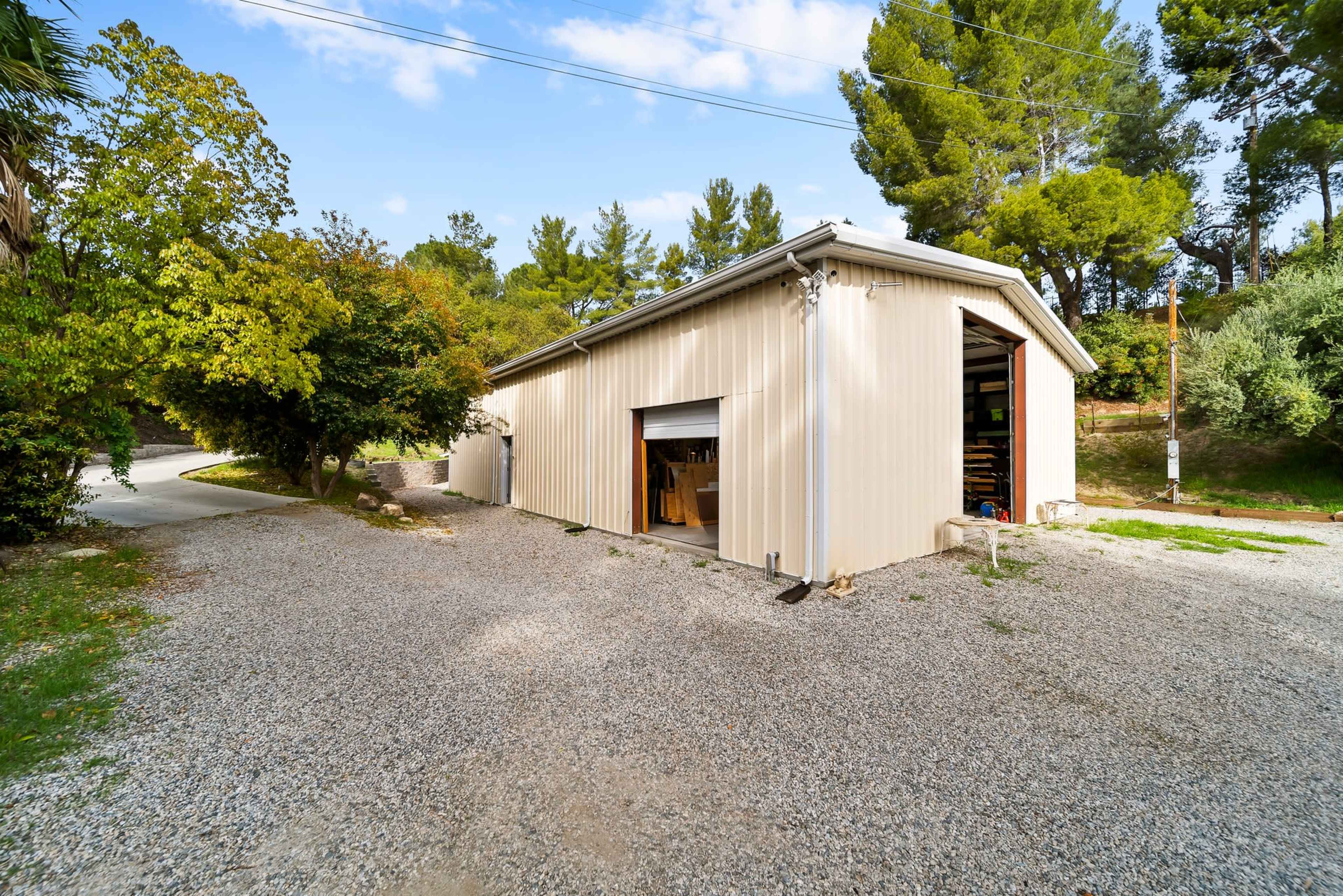 A metal shed is situated on a gravel pathway surrounded by trees and greenery.