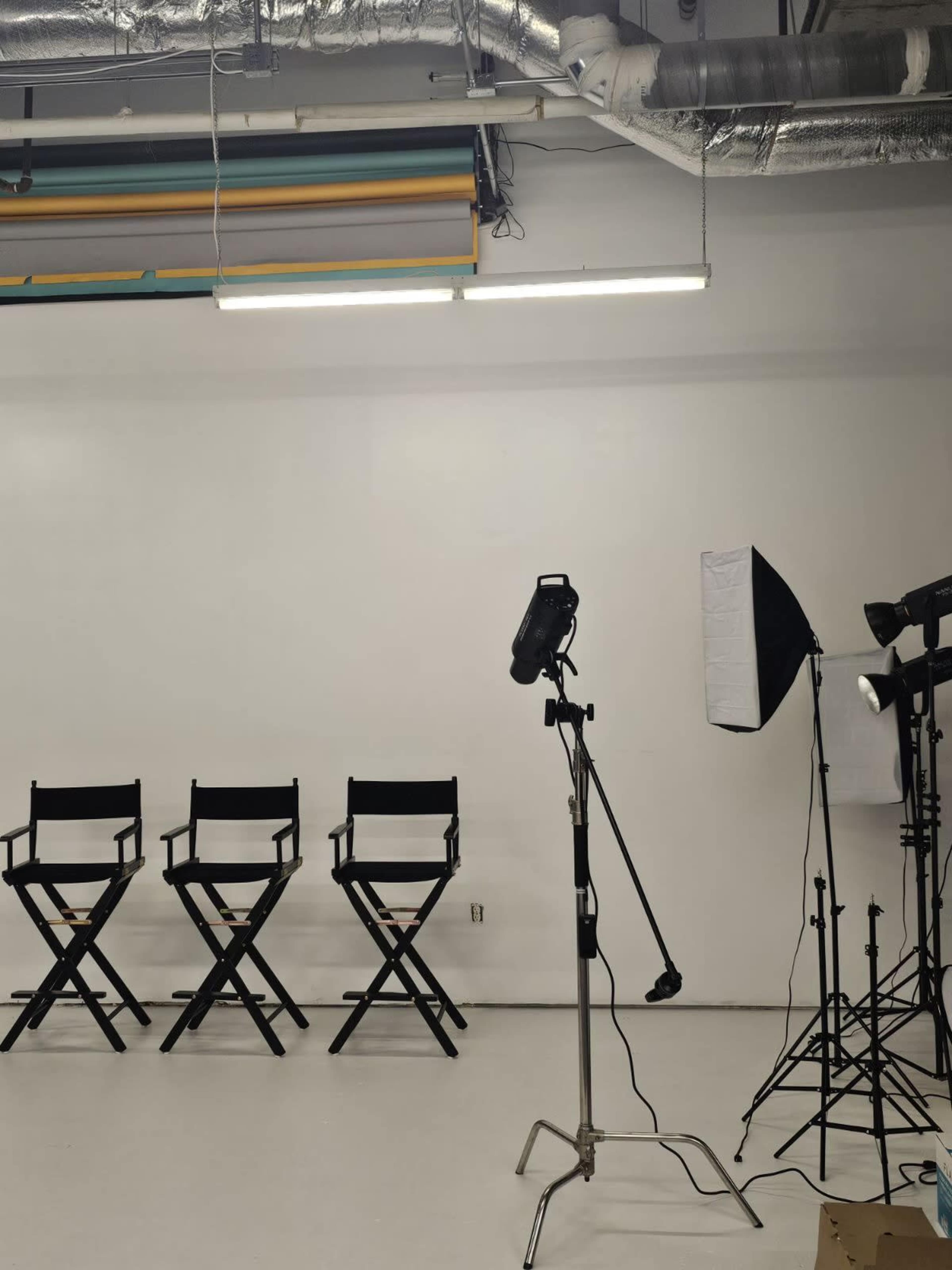 The image depicts an empty studio space with four black director's chairs aligned in front of a backdrop, accompanied by studio lighting equipment.