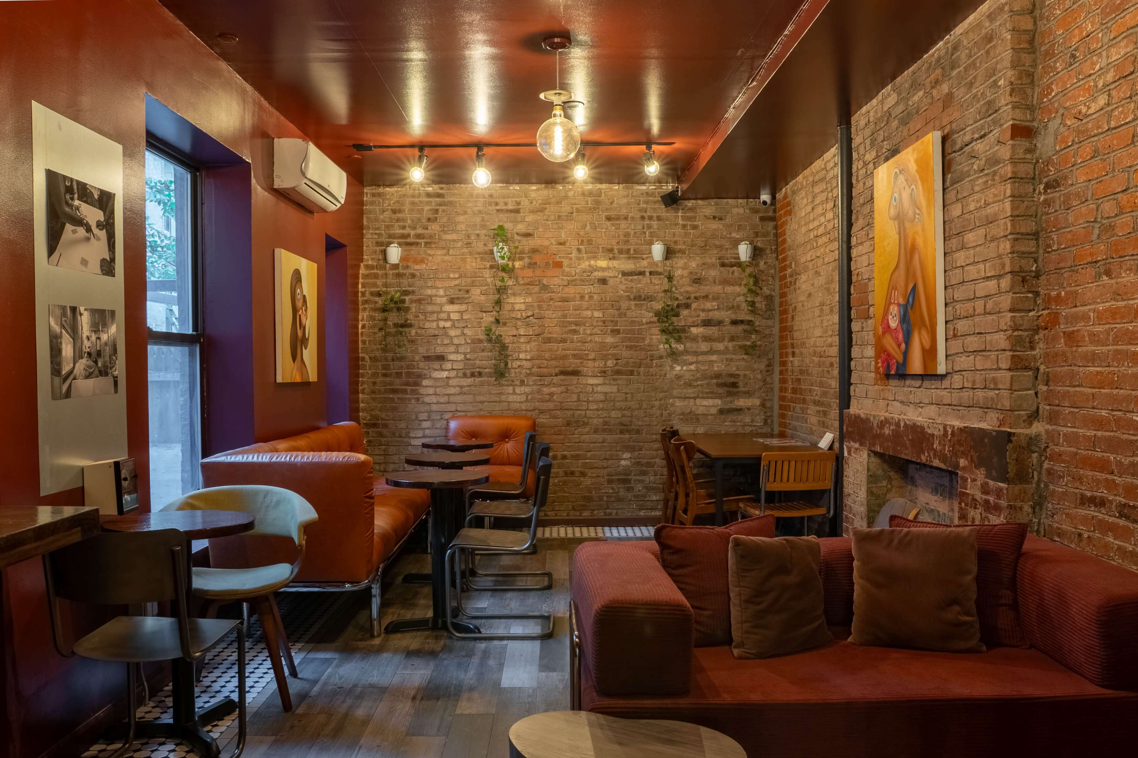 The image shows a cozy lounge area with brick walls, wooden furniture, and colorful artworks on display.