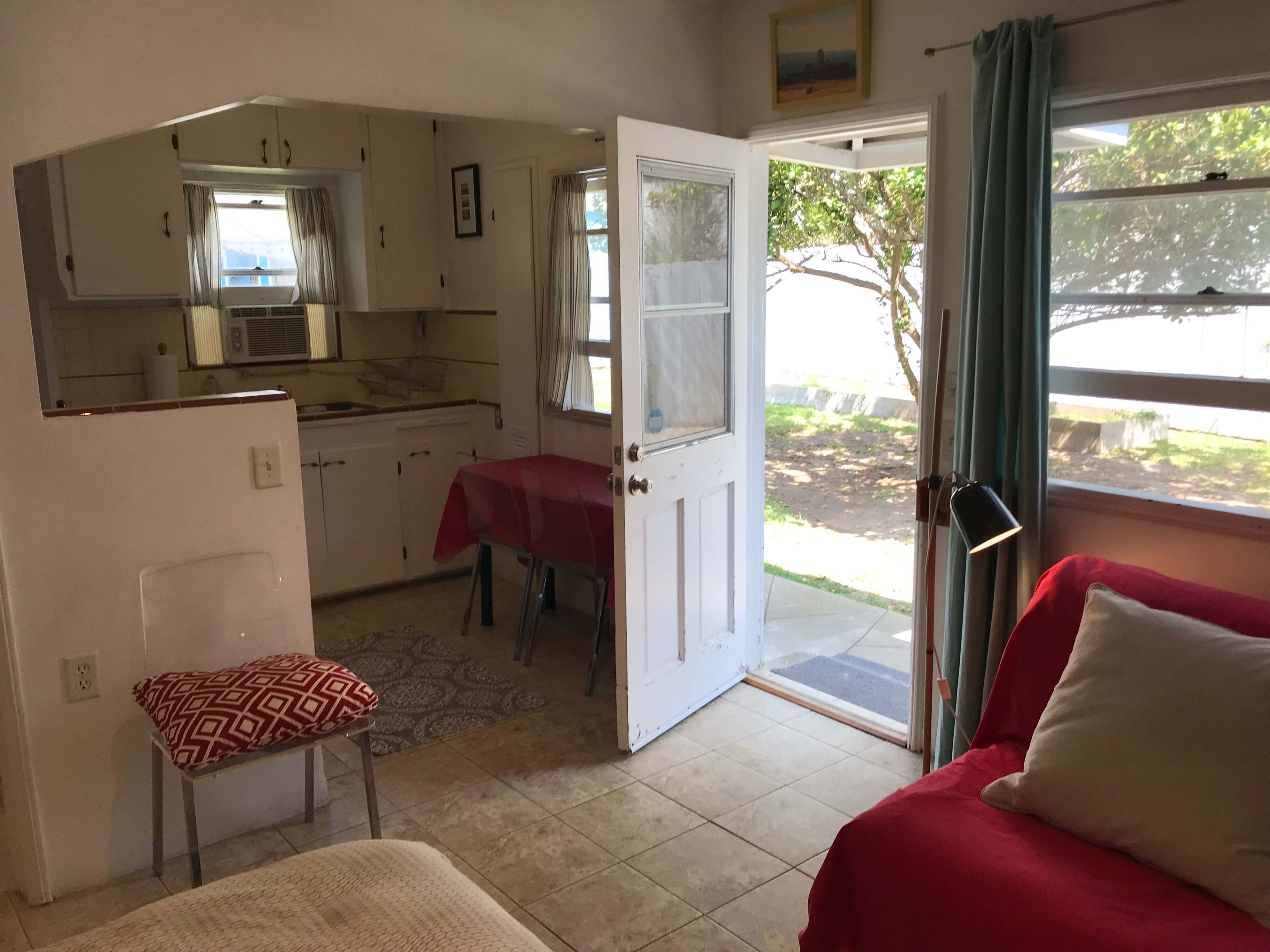 A small, open living space features a kitchen area with a table, a door leading outside, and a seating area with a couch.