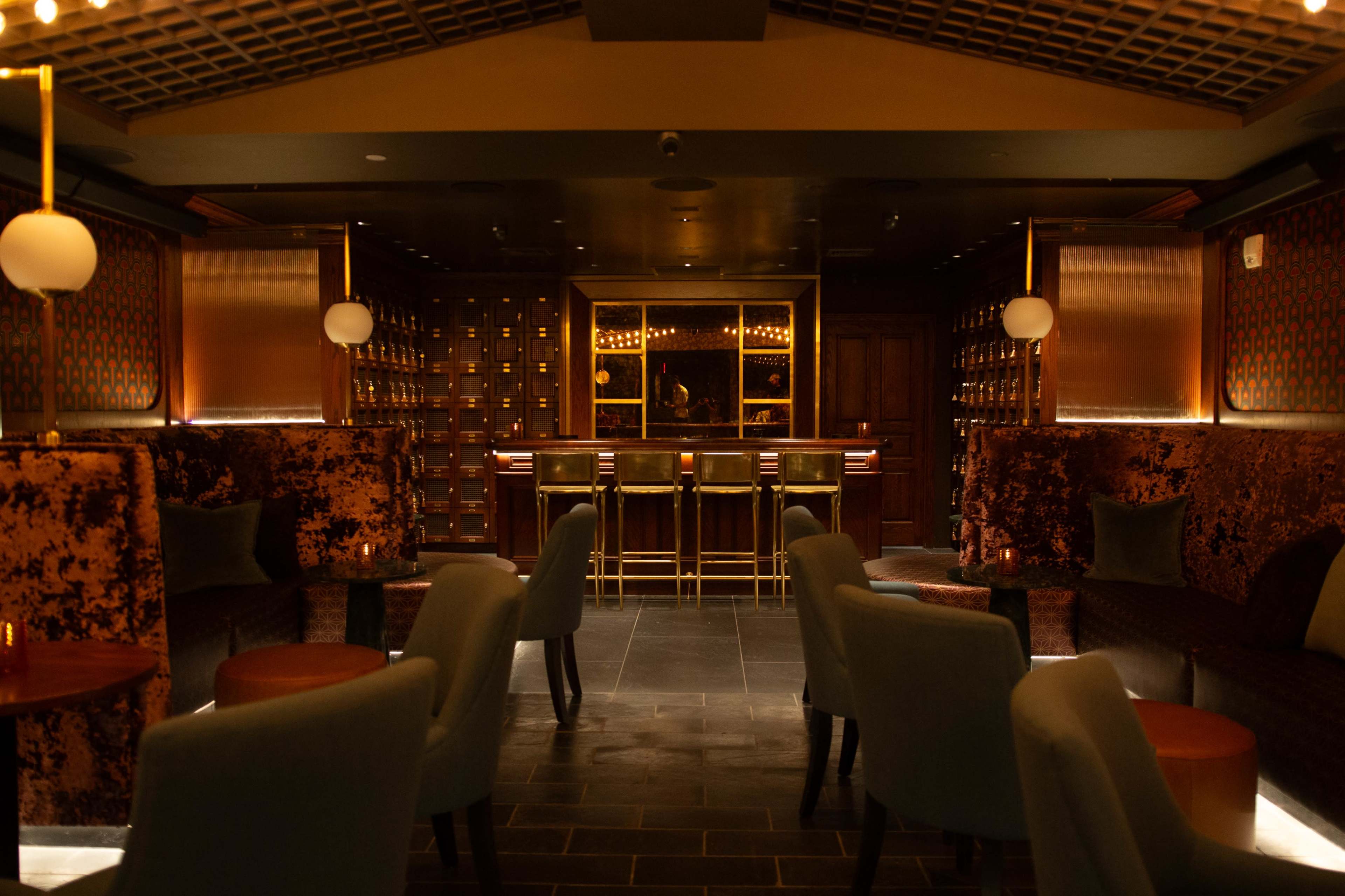 The image shows a dimly lit bar area with plush seating and a well-lit bar counter in the background.