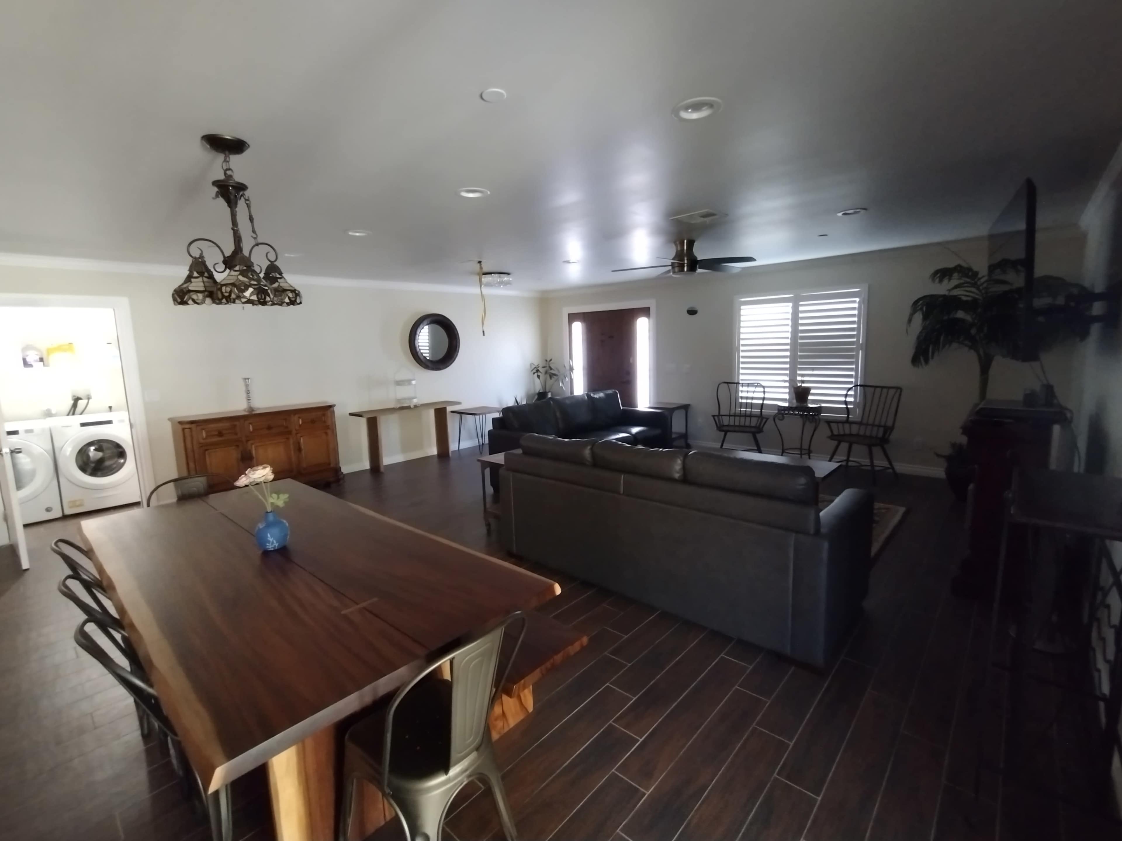 A spacious living area with a dining table, a sofa, and a laundry room visible in the background.