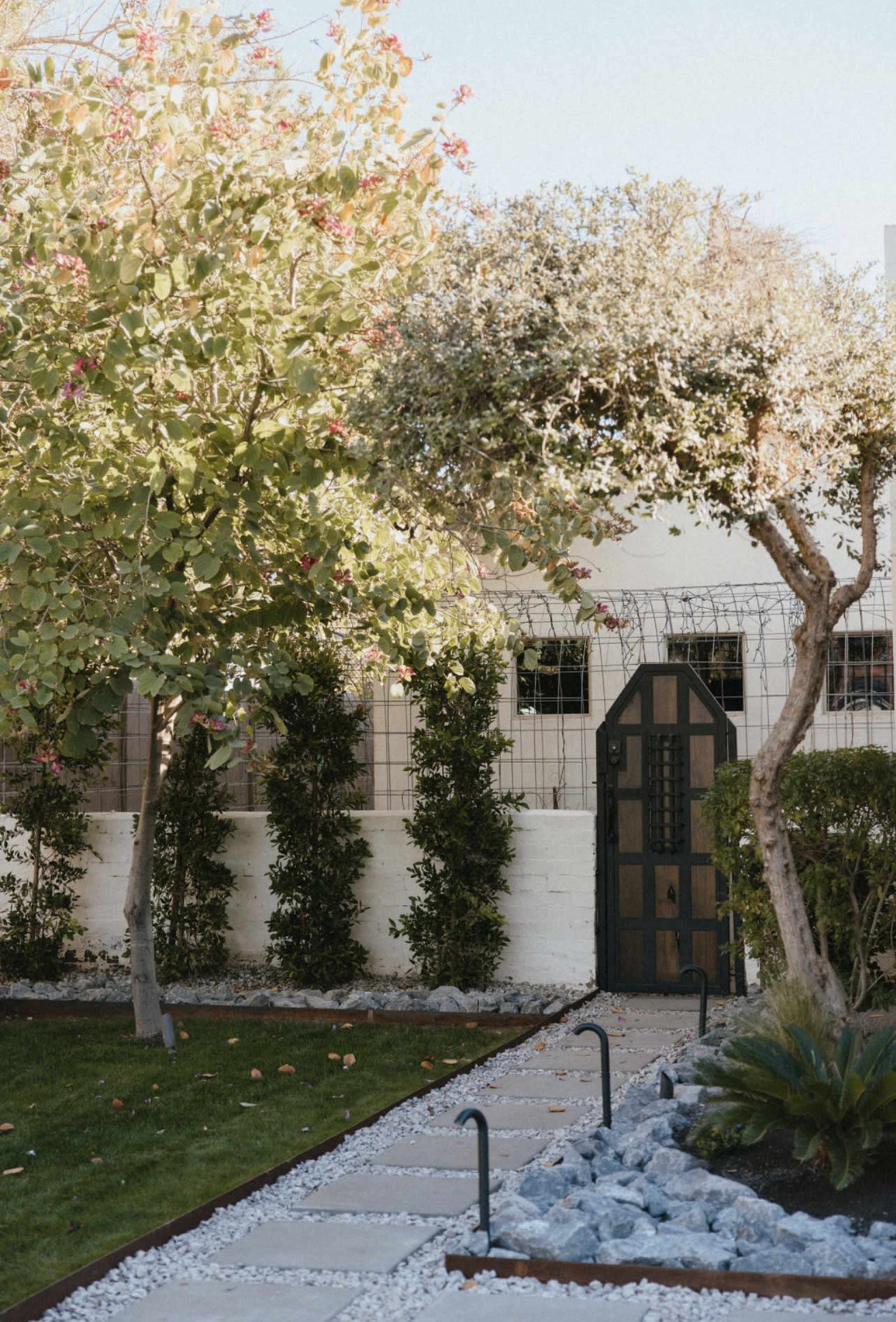 A pathway of stone pavers leads to a green garden with trees and a decorative gate.