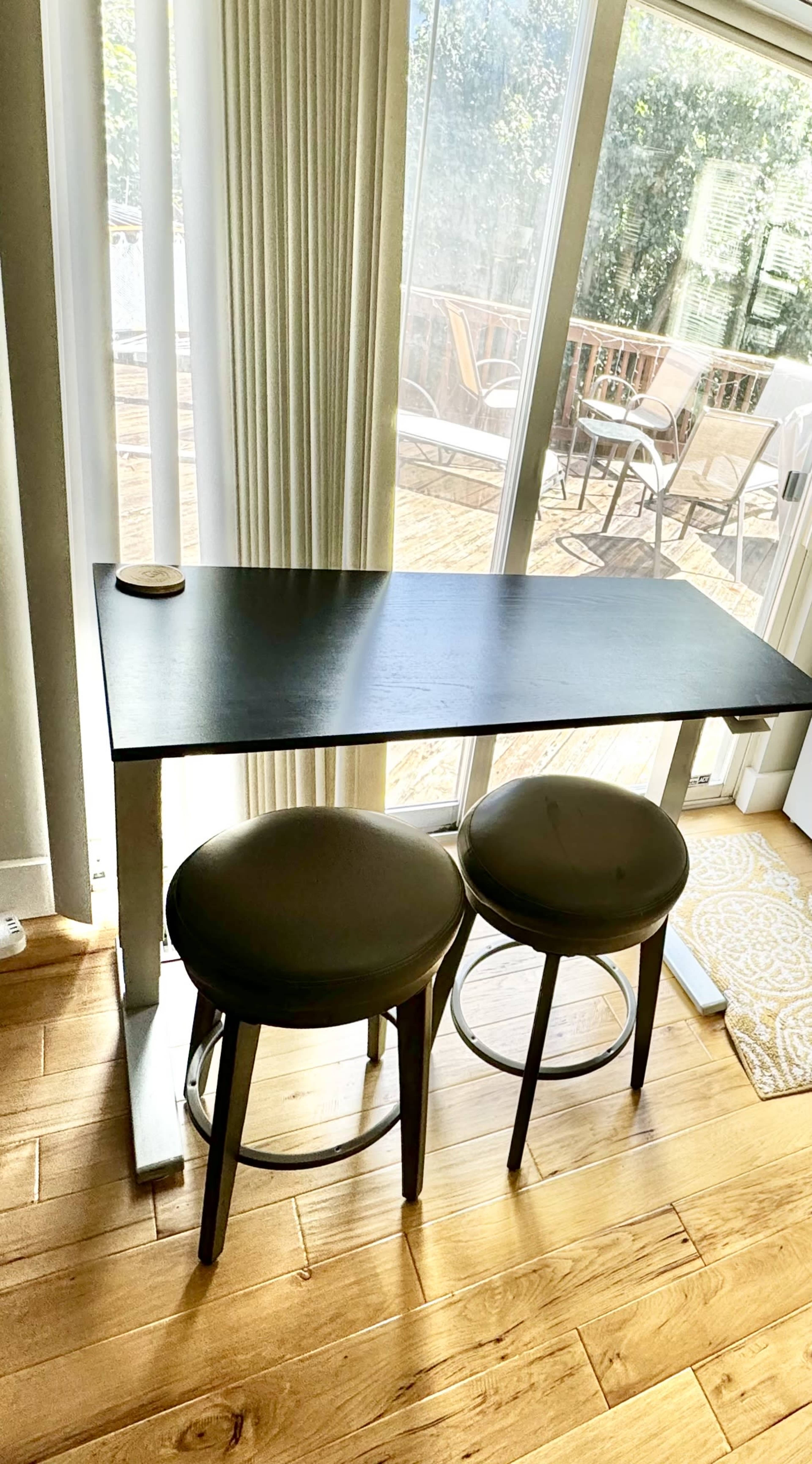 A sleek black table with two round stools sits next to a large window, allowing natural light to illuminate the space.