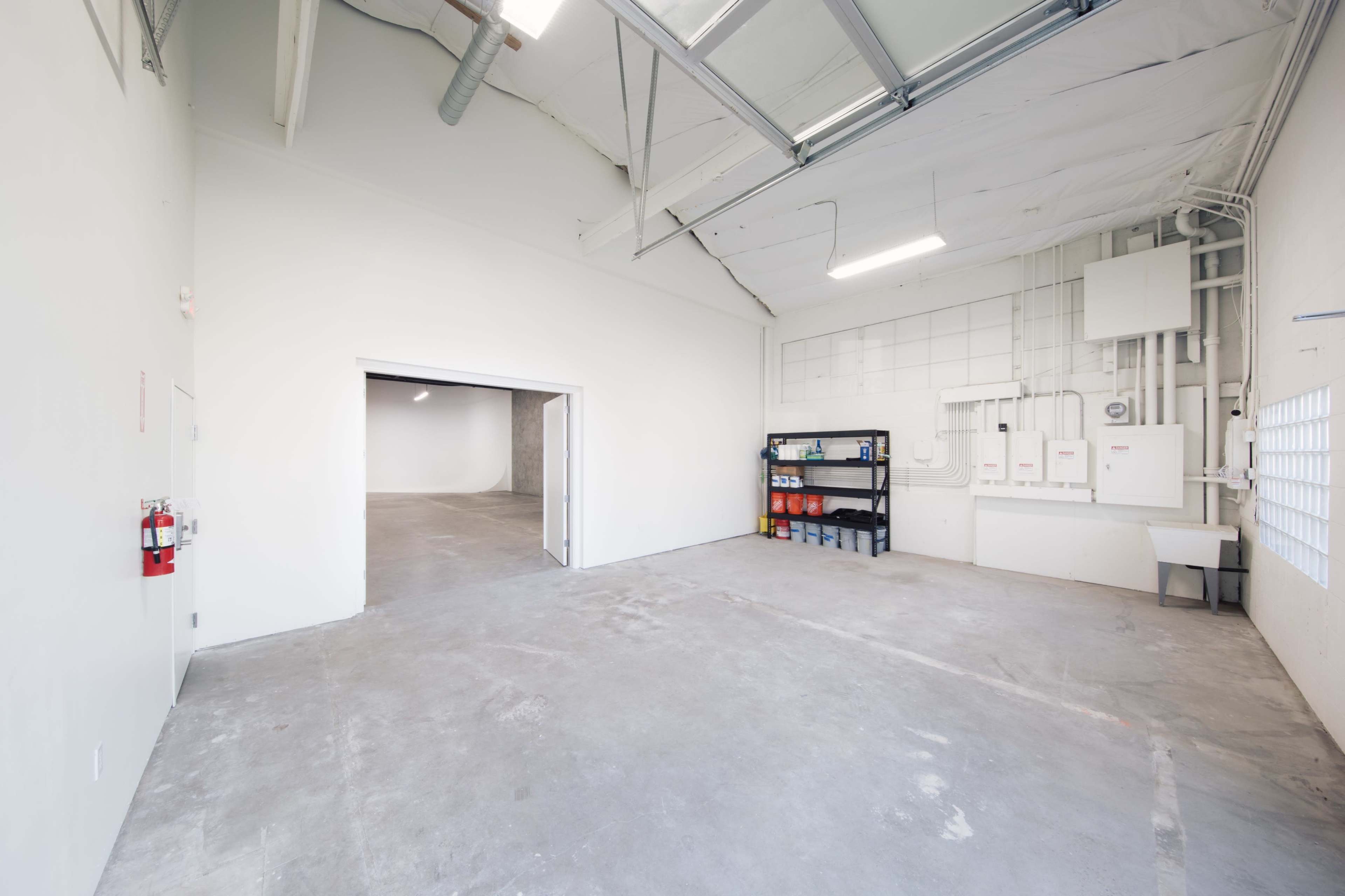 A spacious, empty room with concrete flooring, white walls, and a shelving unit on one side.