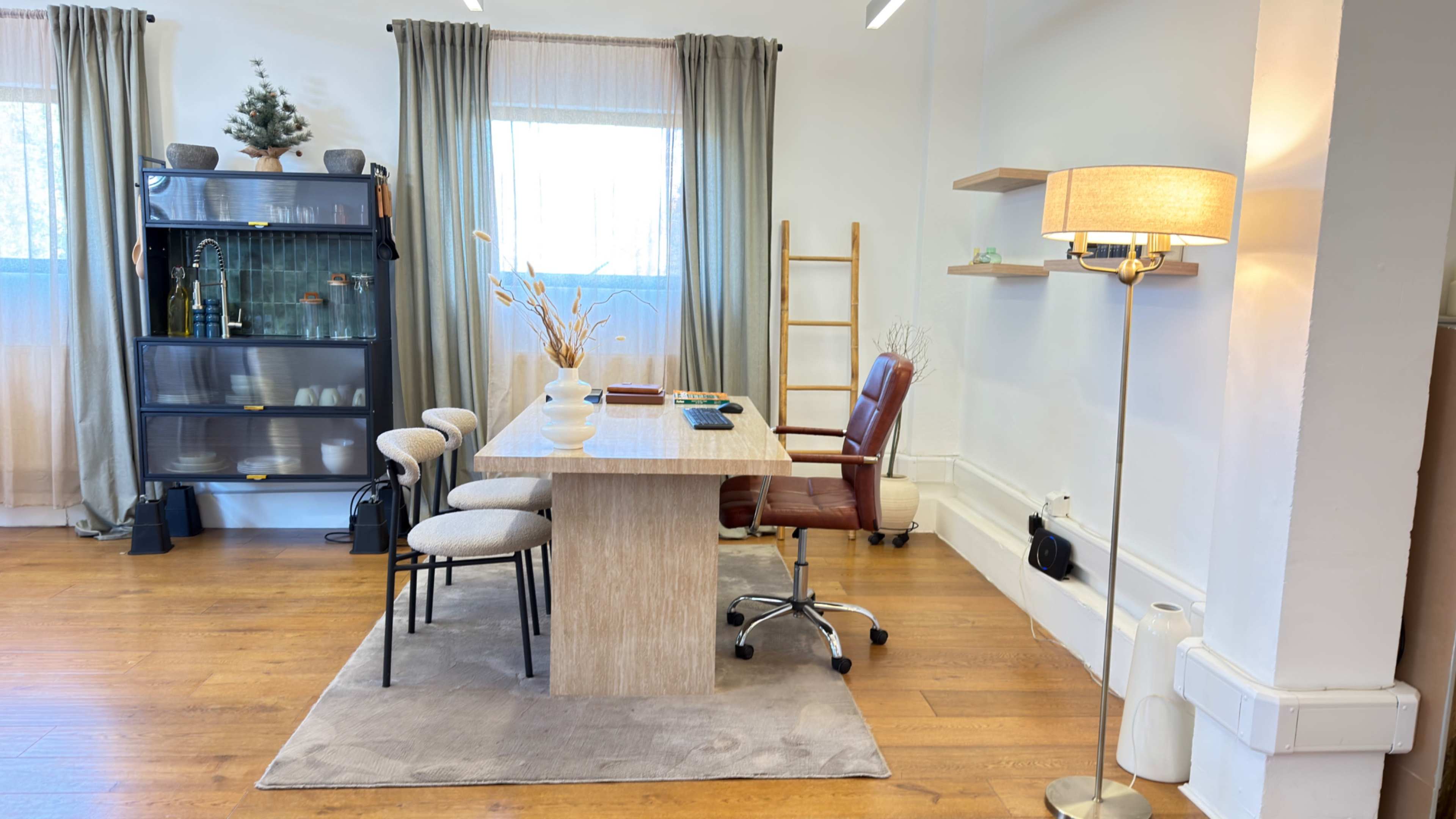 The image shows a modern office space with a wooden table, three chairs, a floor lamp, and a glass cabinet against the wall.