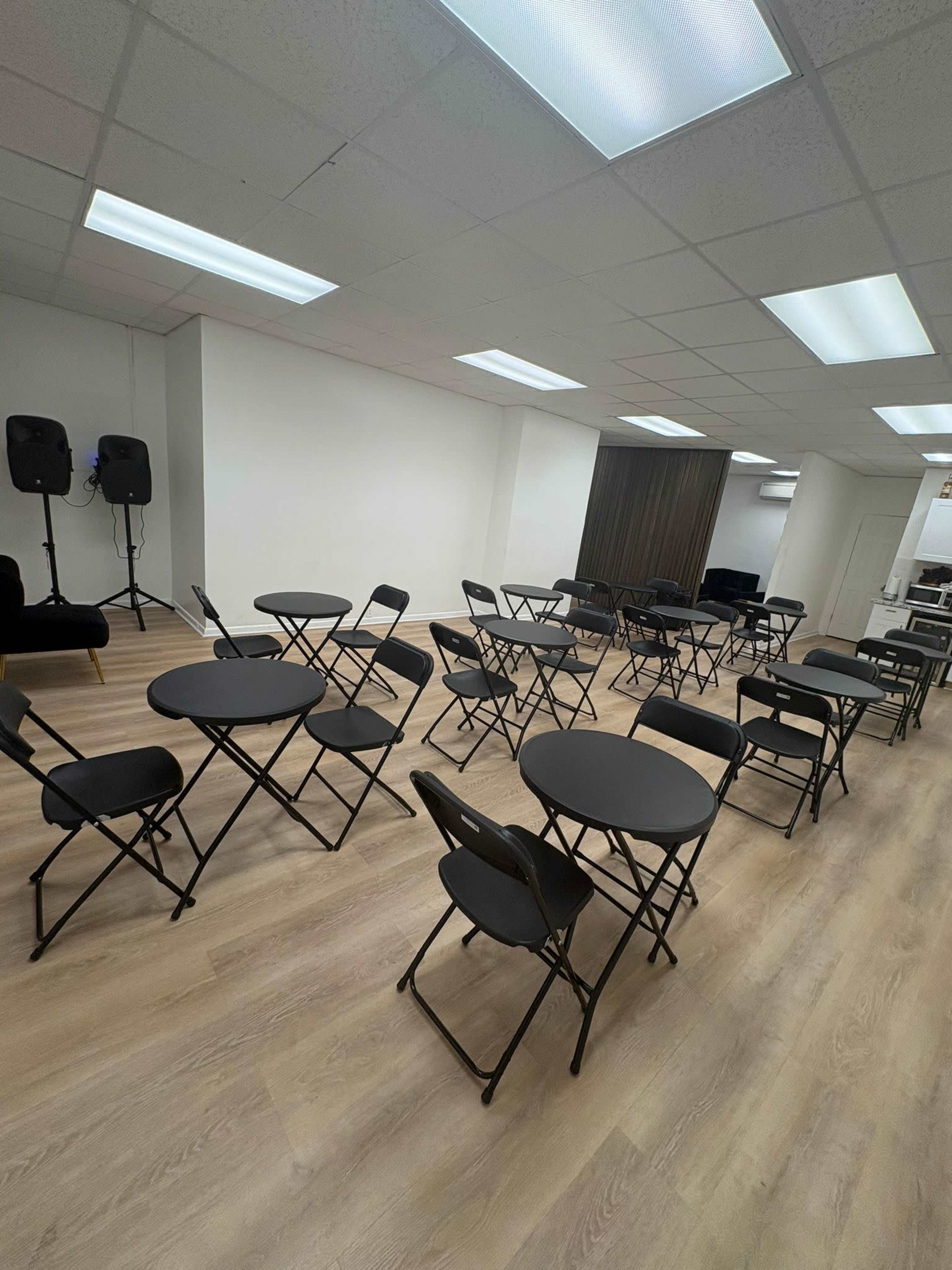 The image shows a room arranged with multiple circular tables and black folding chairs set up in a grid pattern.
