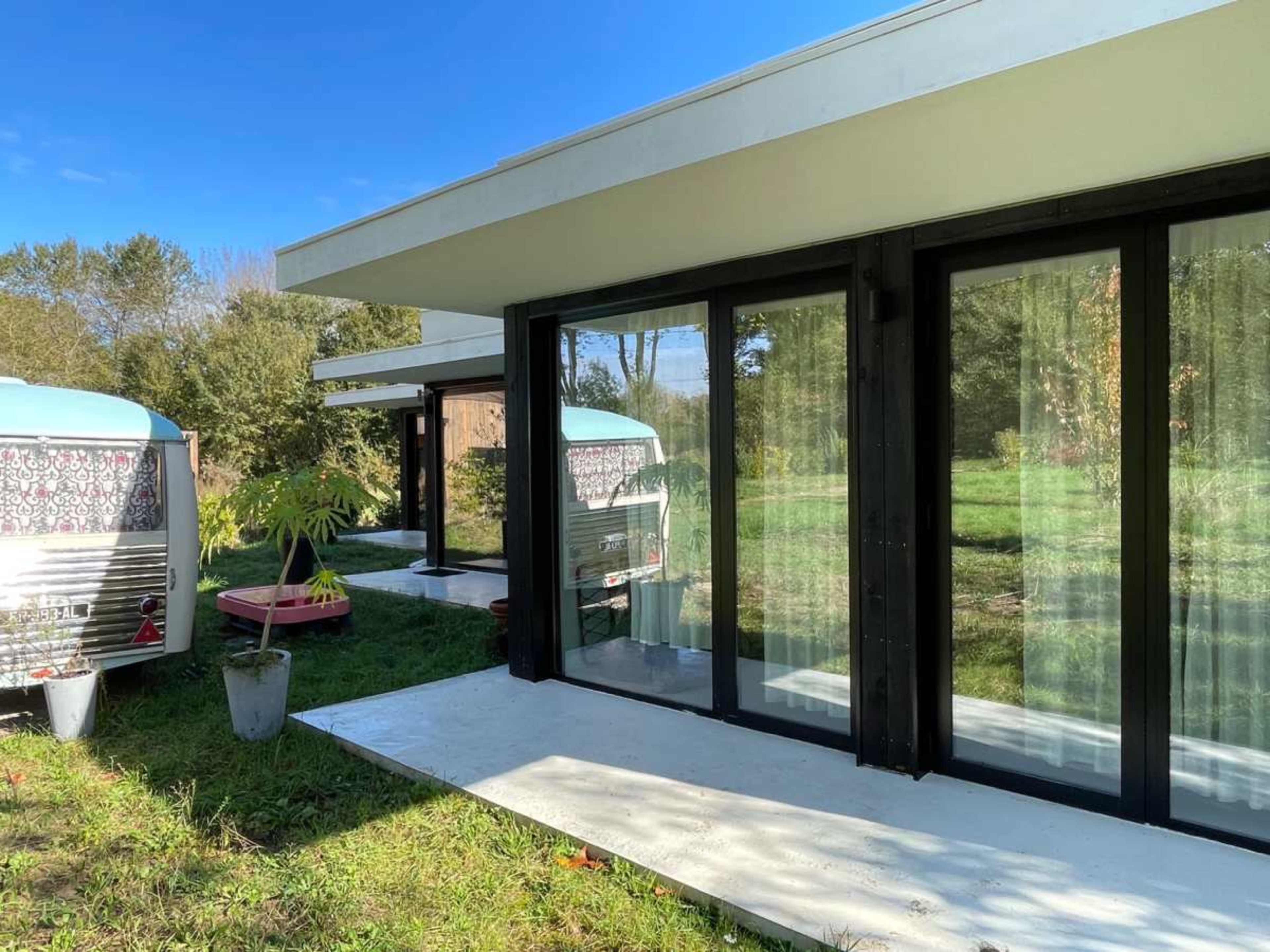 The image shows modern, minimalist houses with large glass windows set against a green landscape.