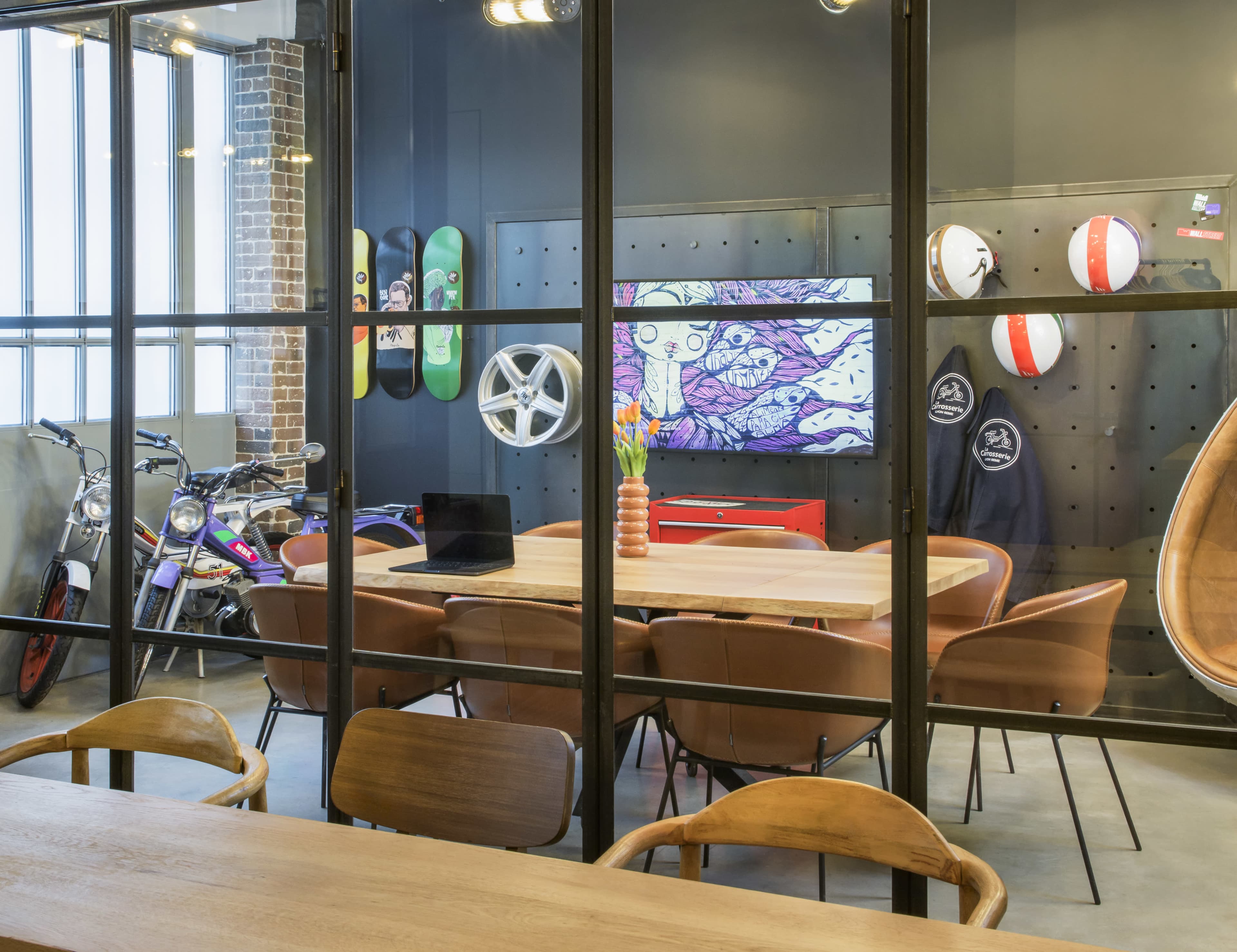 A modern conference room features a large wooden table surrounded by brown chairs, with bikes displayed nearby and a colorful TV screen mounted on the wall.