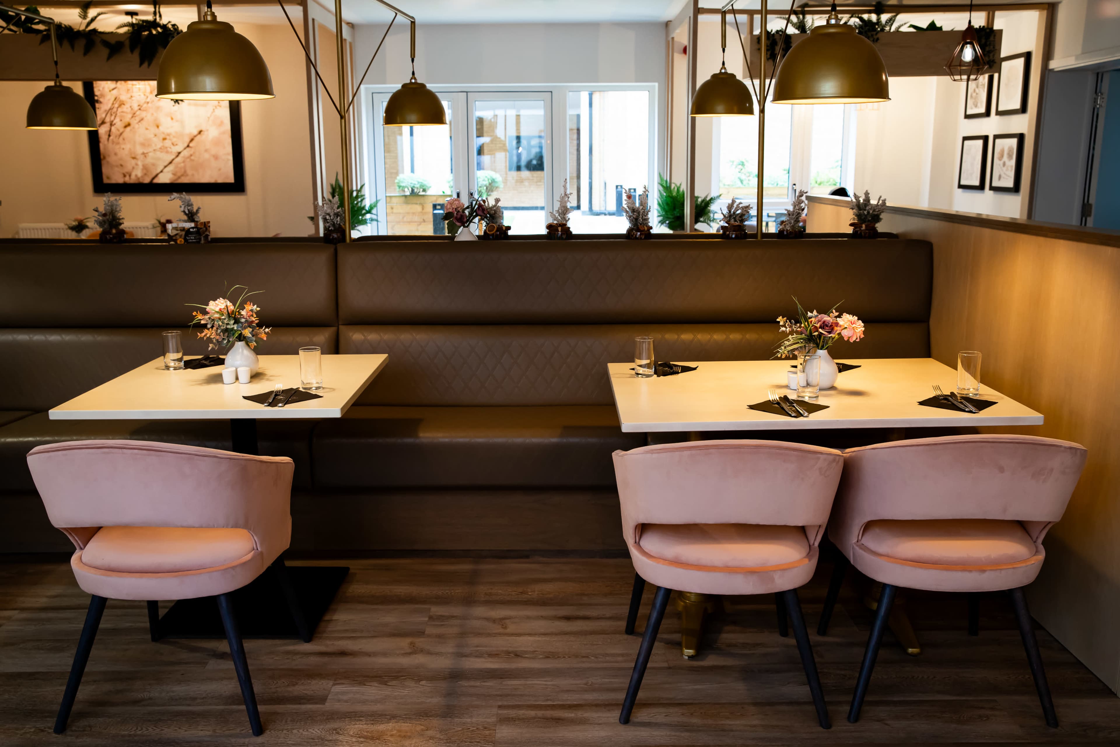 A modern dining area with two tables set for meals, featuring elegant floral centerpieces and upholstered chairs.