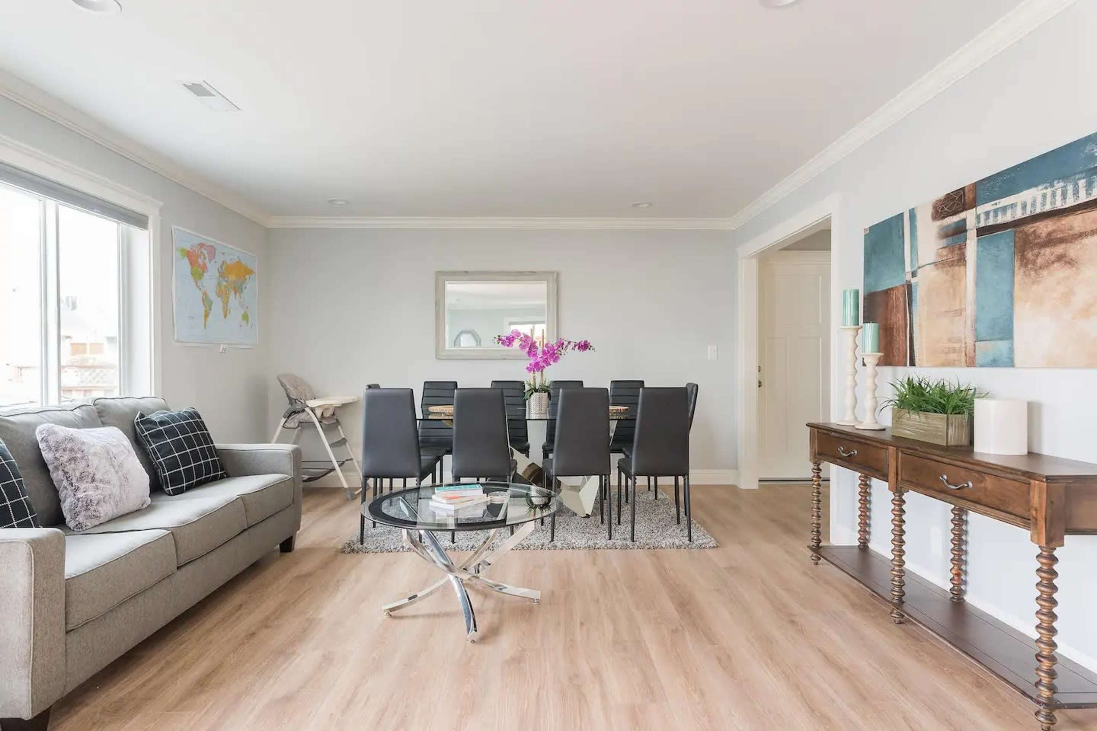 A modern living room features a gray sofa, a glass coffee table, and a dining area with a large table surrounded by black chairs.