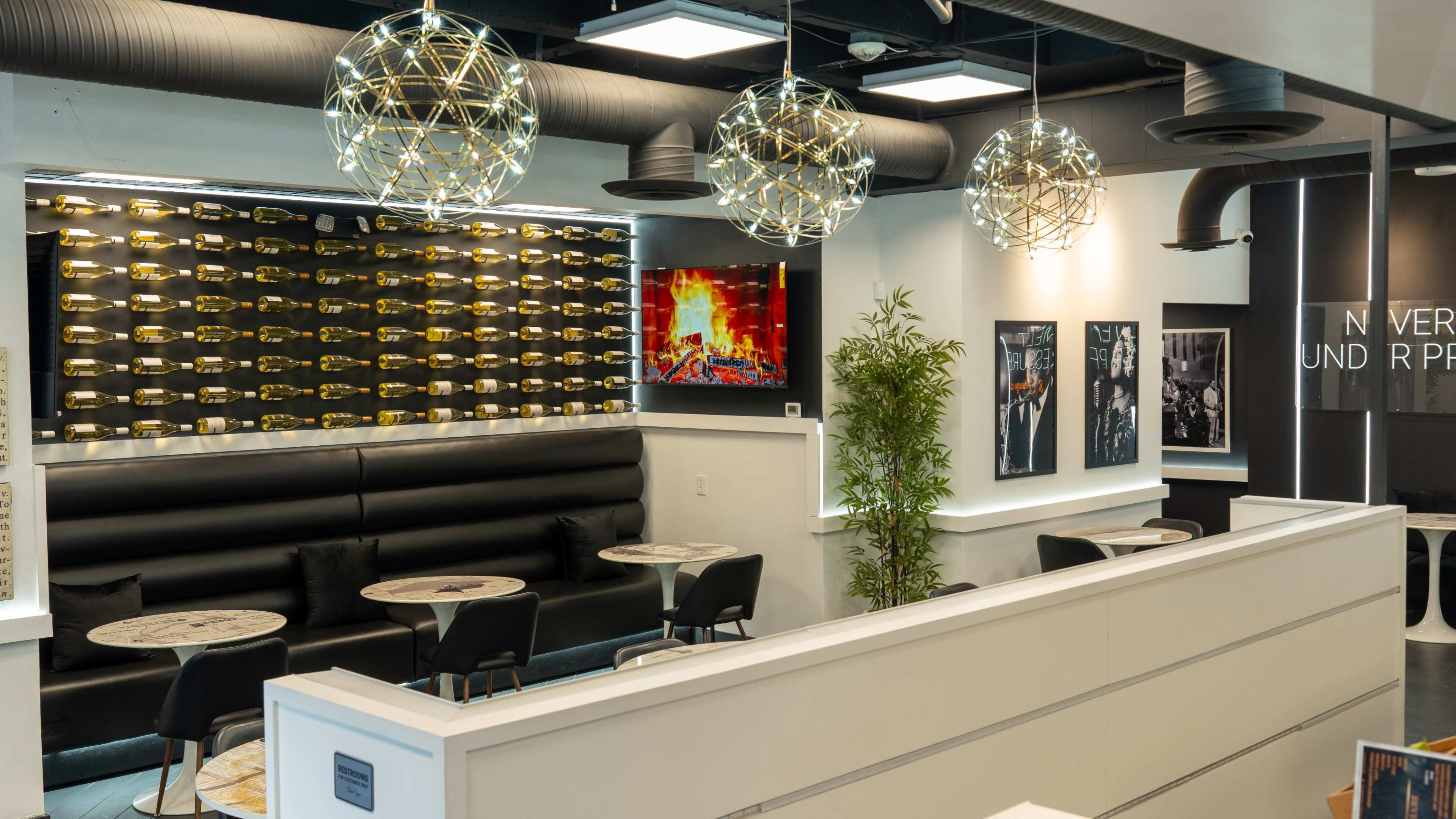 The image shows a modern café interior featuring sleek black seating, round tables, decorative pendant lights, and a wall adorned with a unique pattern.