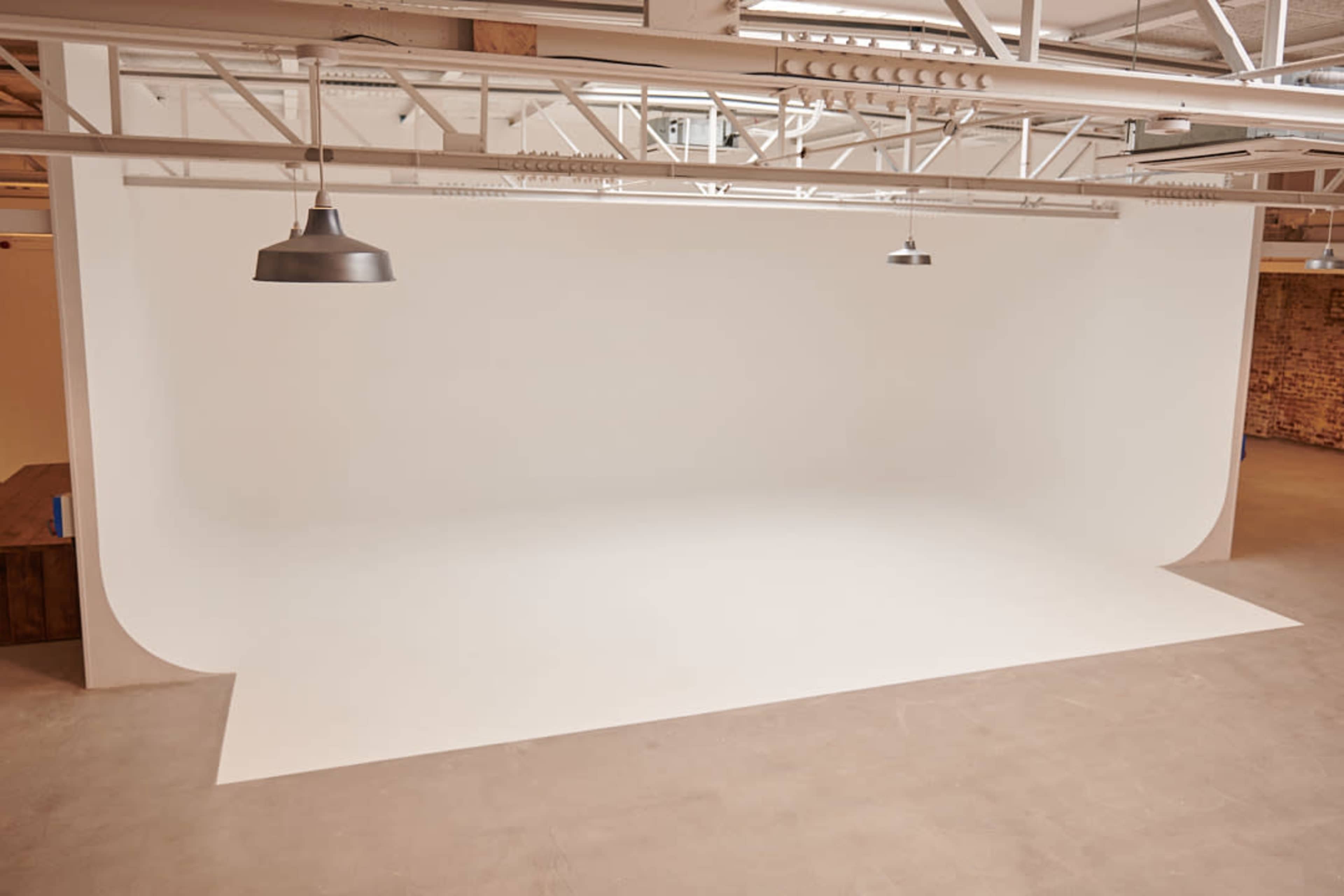 The image shows a spacious studio with a seamless white backdrop and industrial-style lighting overhead.