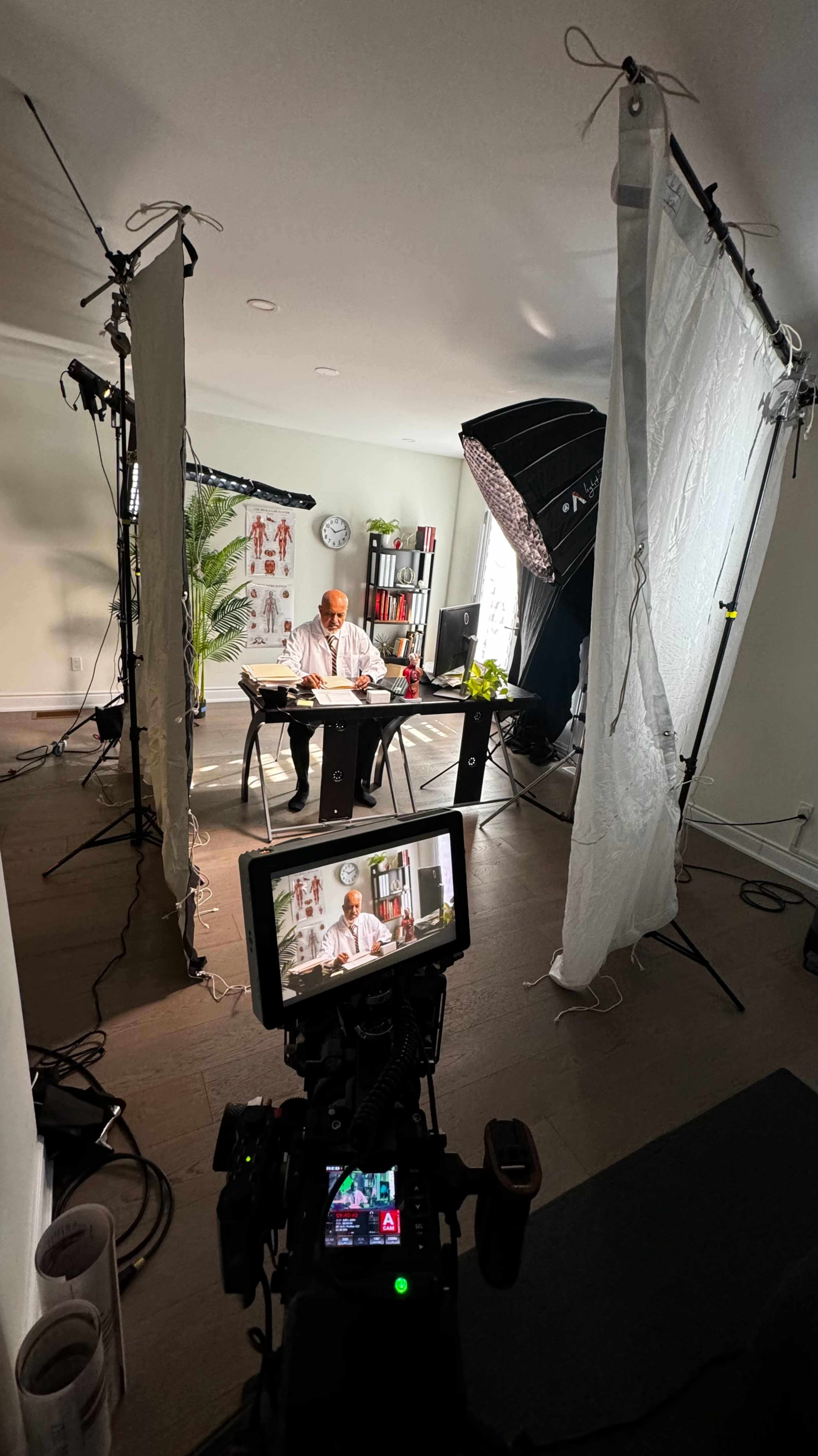 A person is seated at a table in a well-lit room, surrounded by camera equipment and backdrop materials.