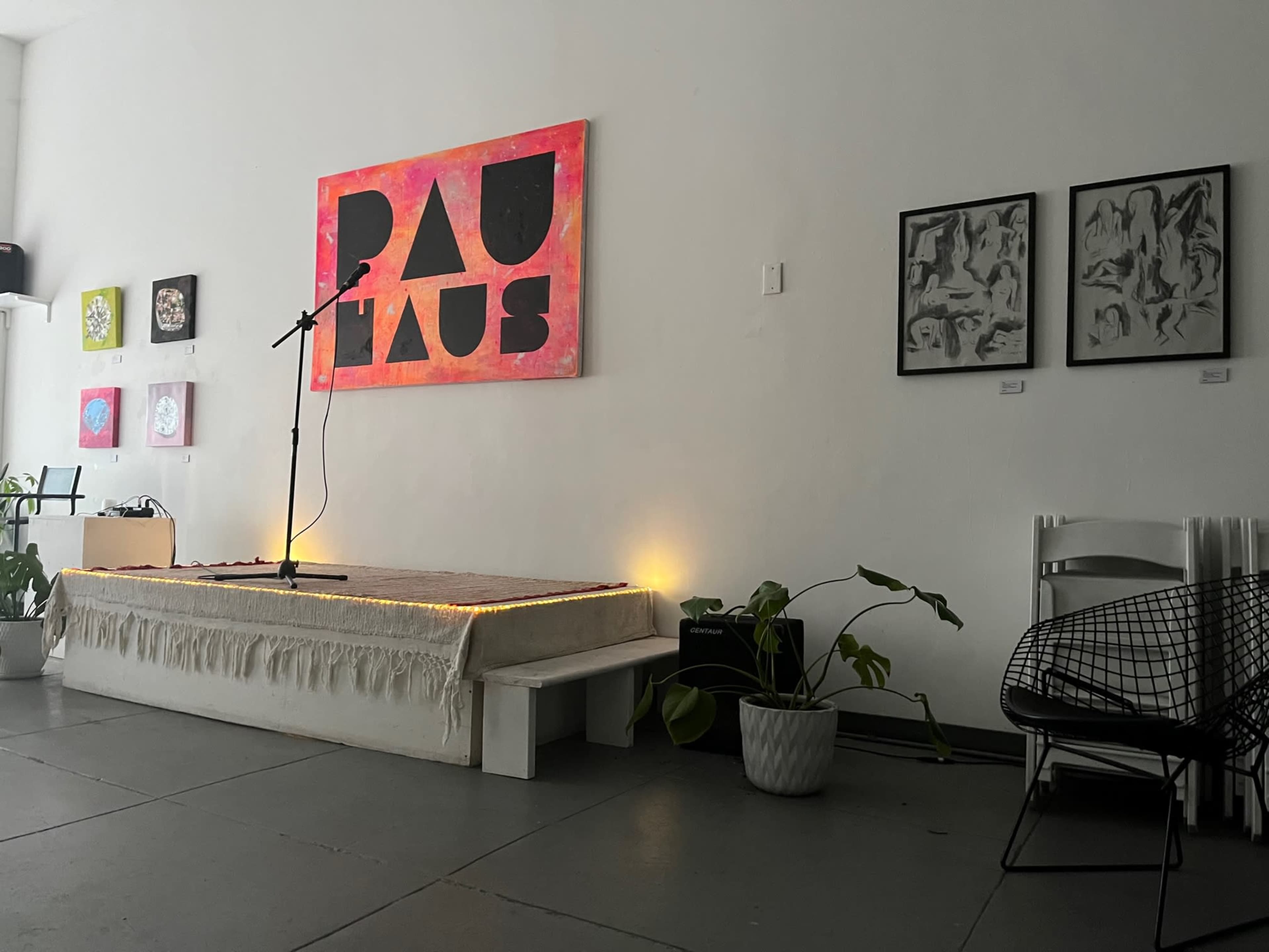 A performance space with a microphone on a small stage, surrounded by artistic wall hangings and potted plants.