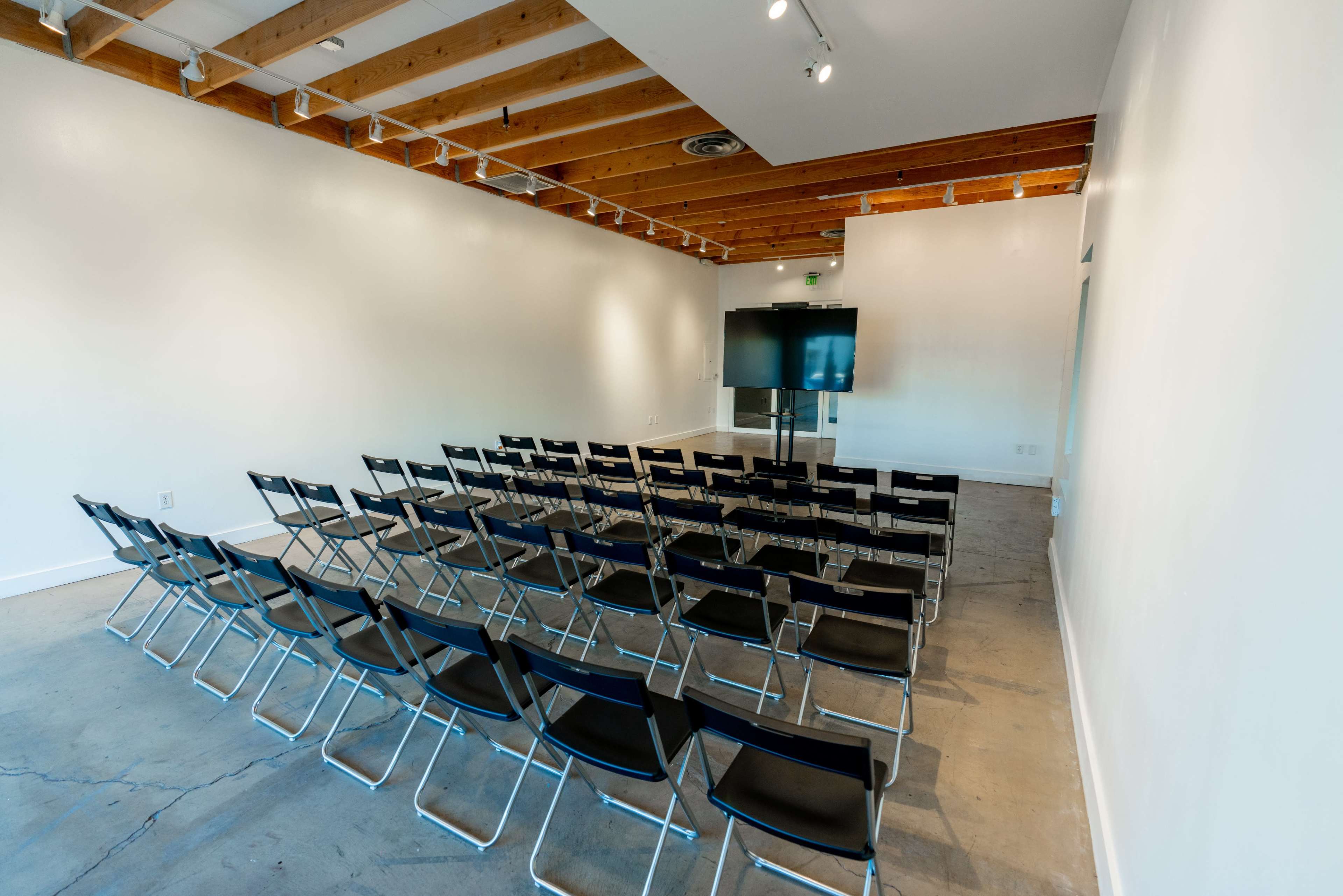 A conference room features rows of black chairs facing a large screen against a white wall.