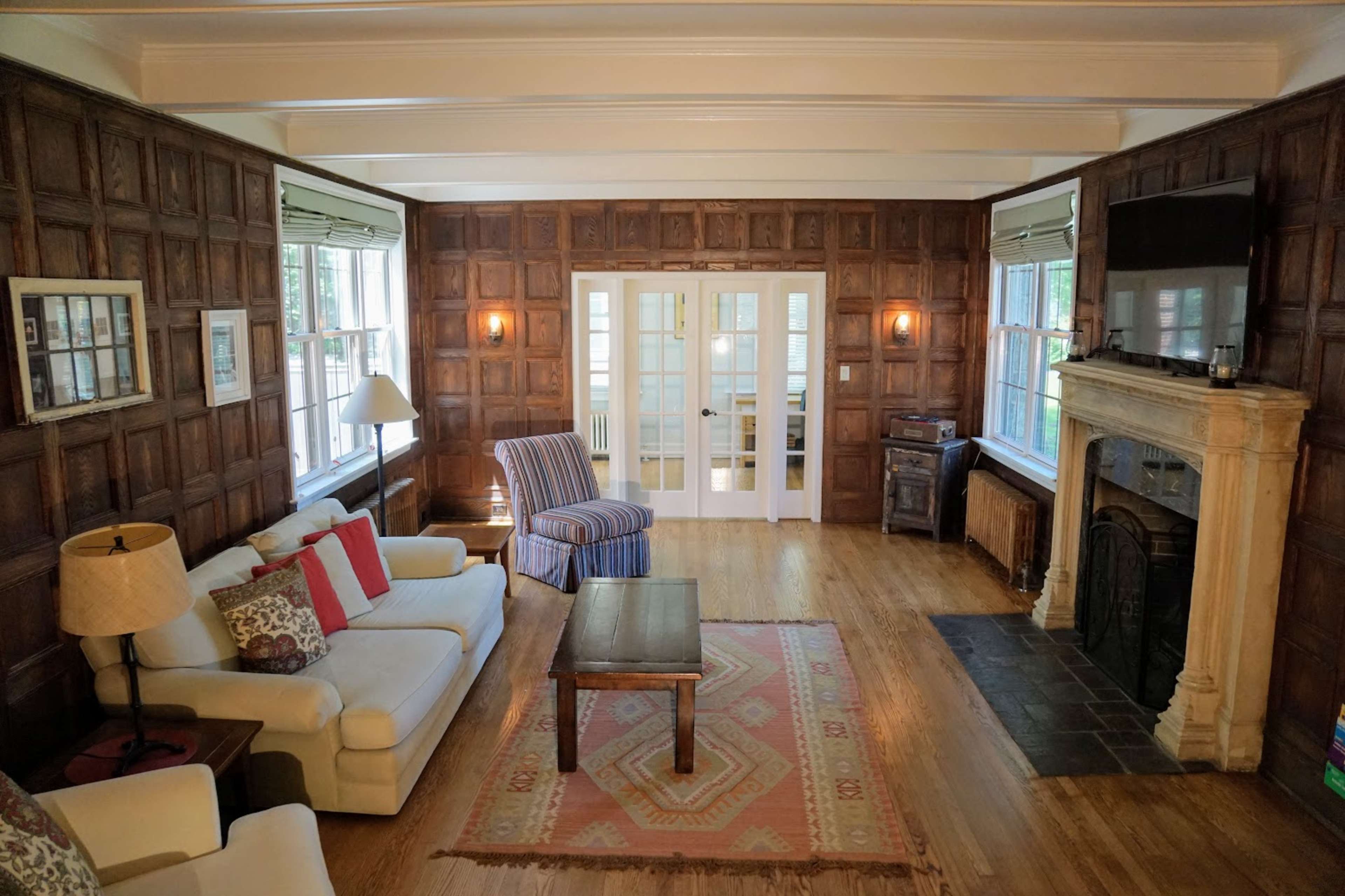 The image shows a living room with wooden paneled walls, a fireplace, a coffee table, and two sofas arranged around the space.