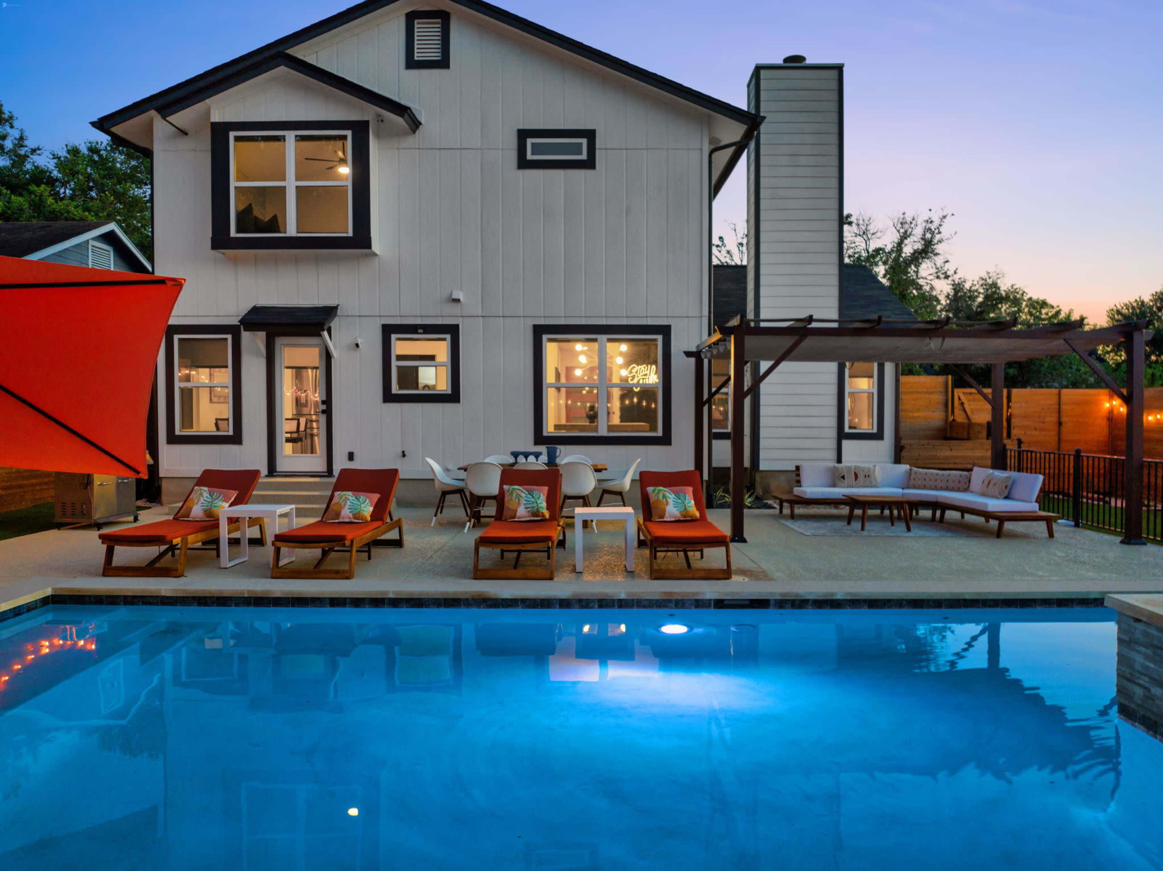 A modern two-story house with a pool features lounge chairs and an outdoor seating area.
