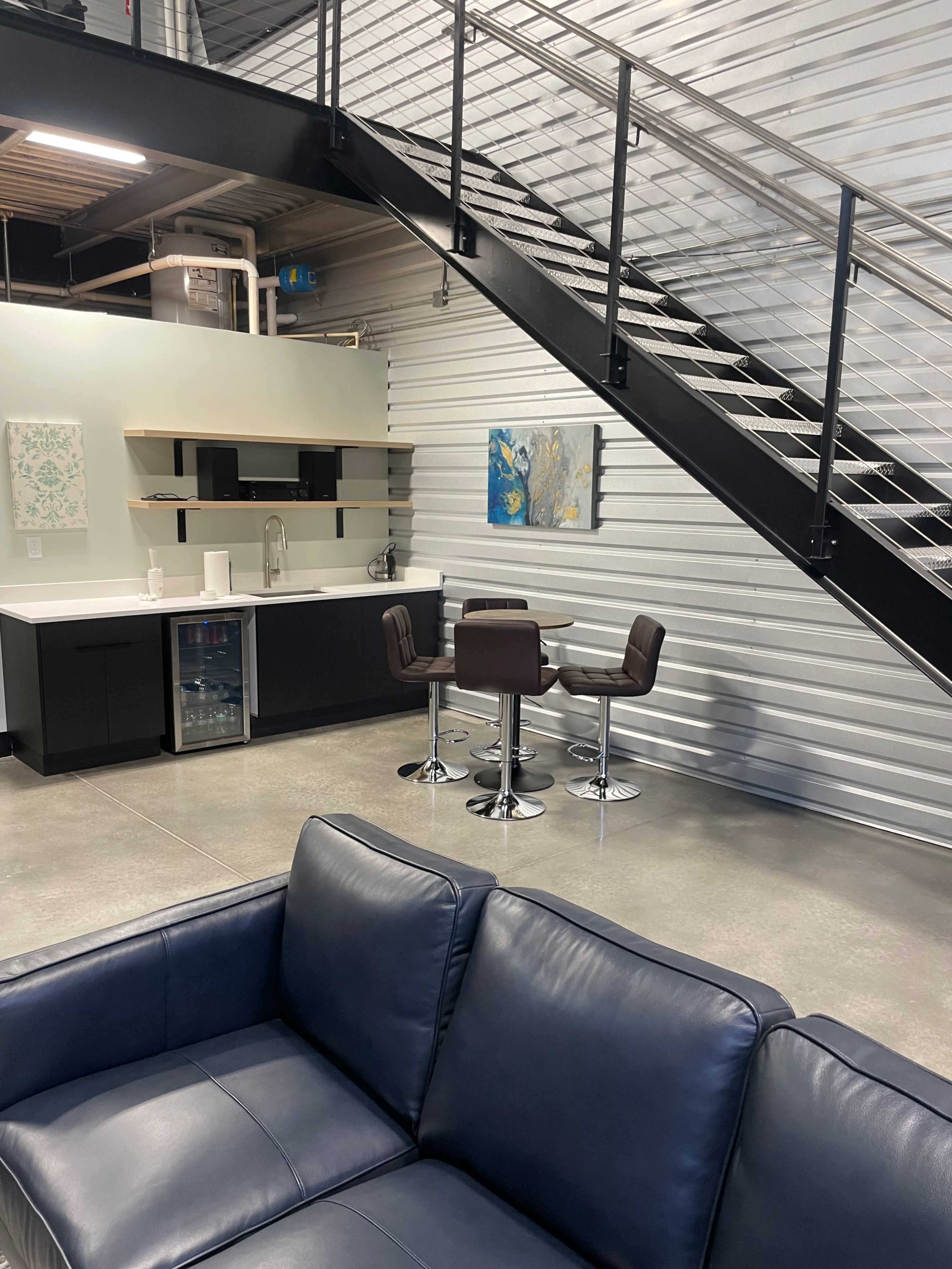 The image shows a contemporary interior space featuring a kitchen area, a dining table with four chairs, and a modern staircase leading to an upper level.