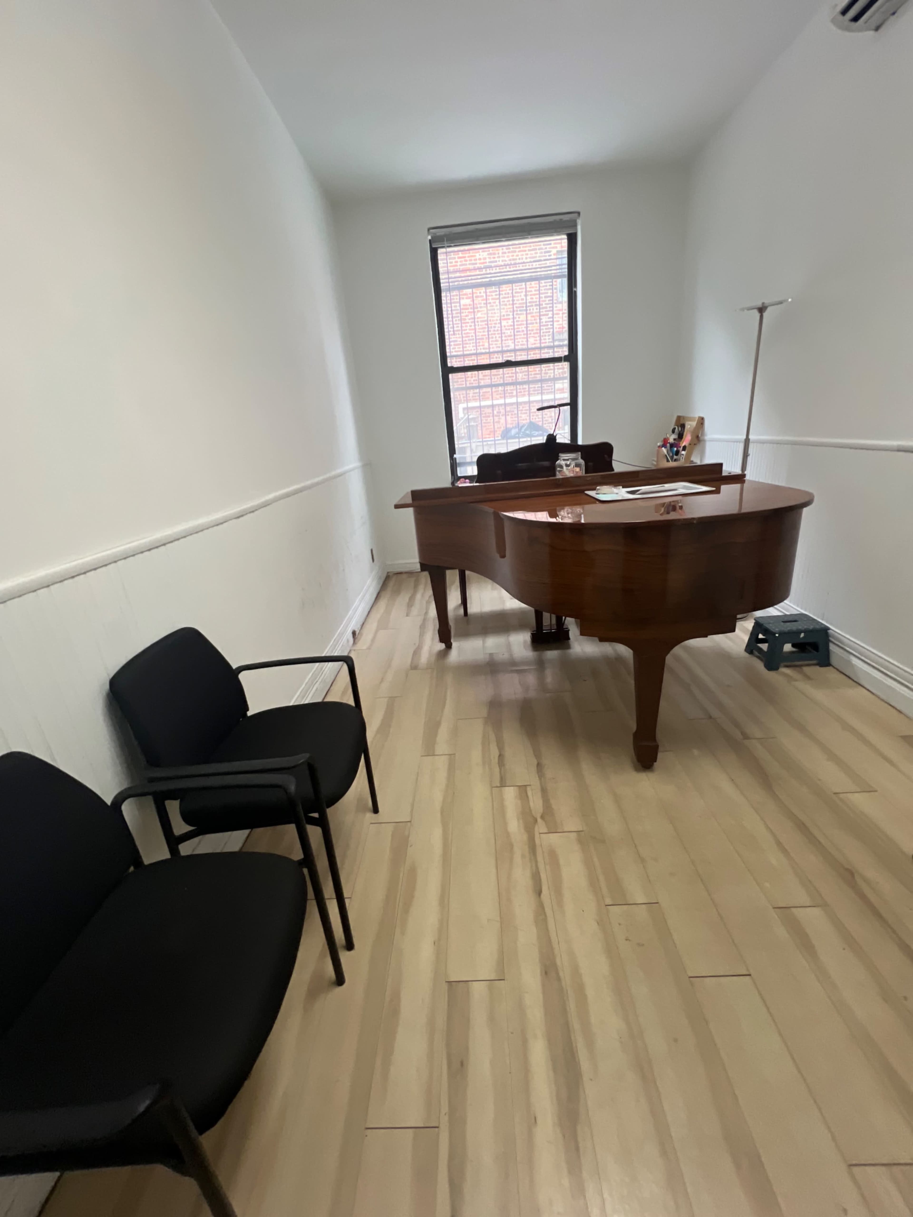 The image shows a minimalistic office space featuring a wooden desk, two black chairs, and a window allowing natural light.