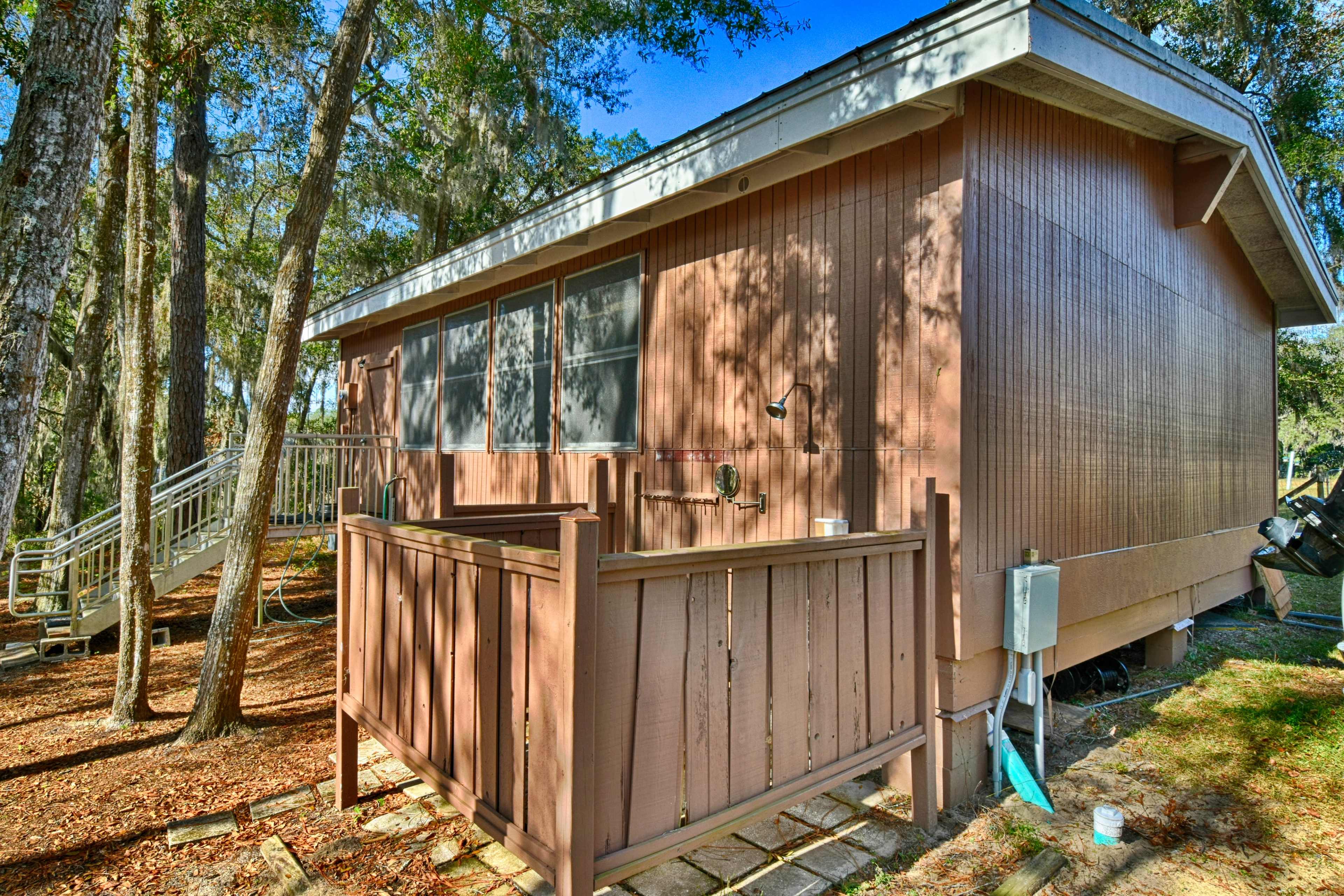 The side of a wooden cabin with a small deck and surrounded by trees.