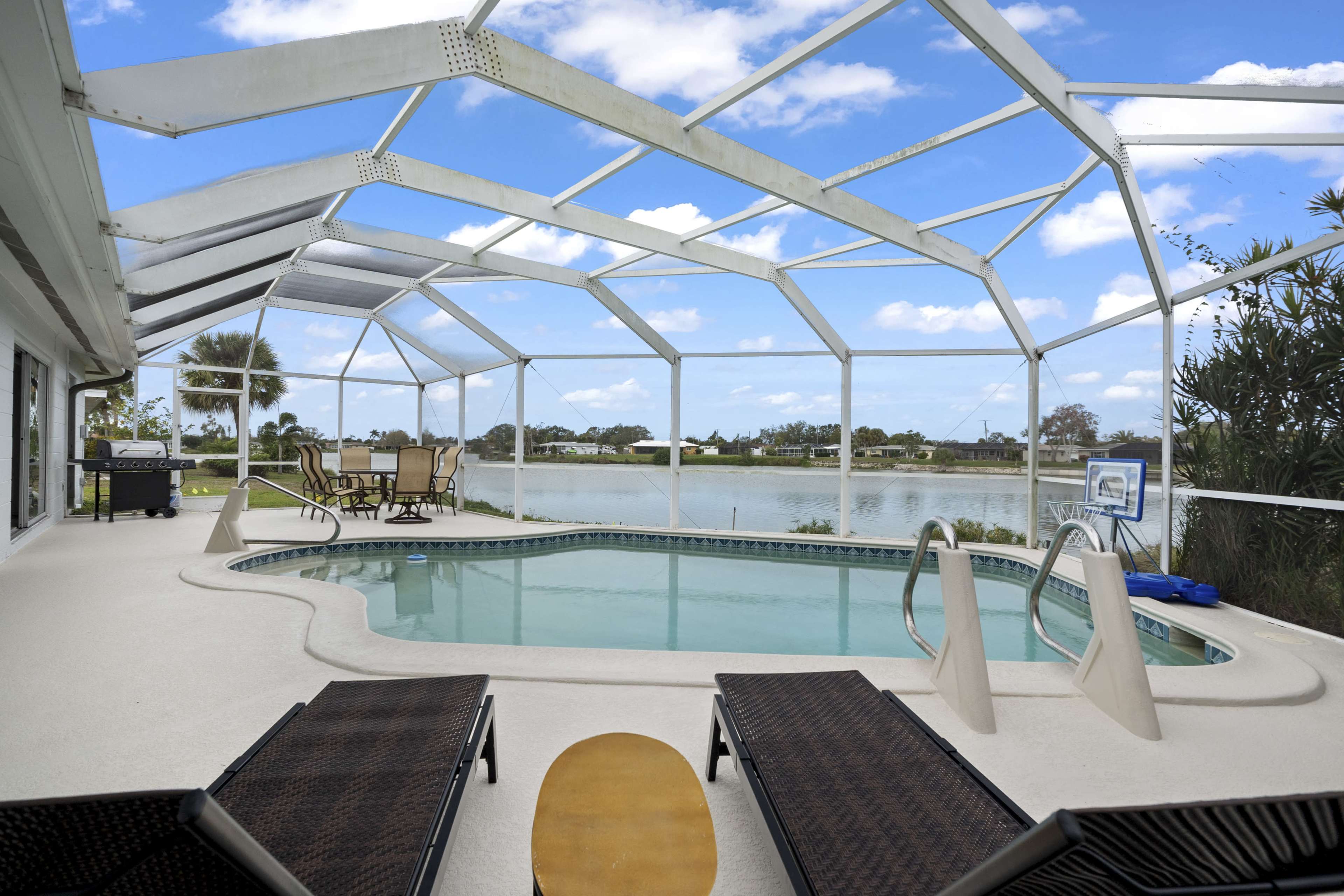A screened-in patio features a swimming pool with two lounge chairs and a view of a lake and blue sky.
