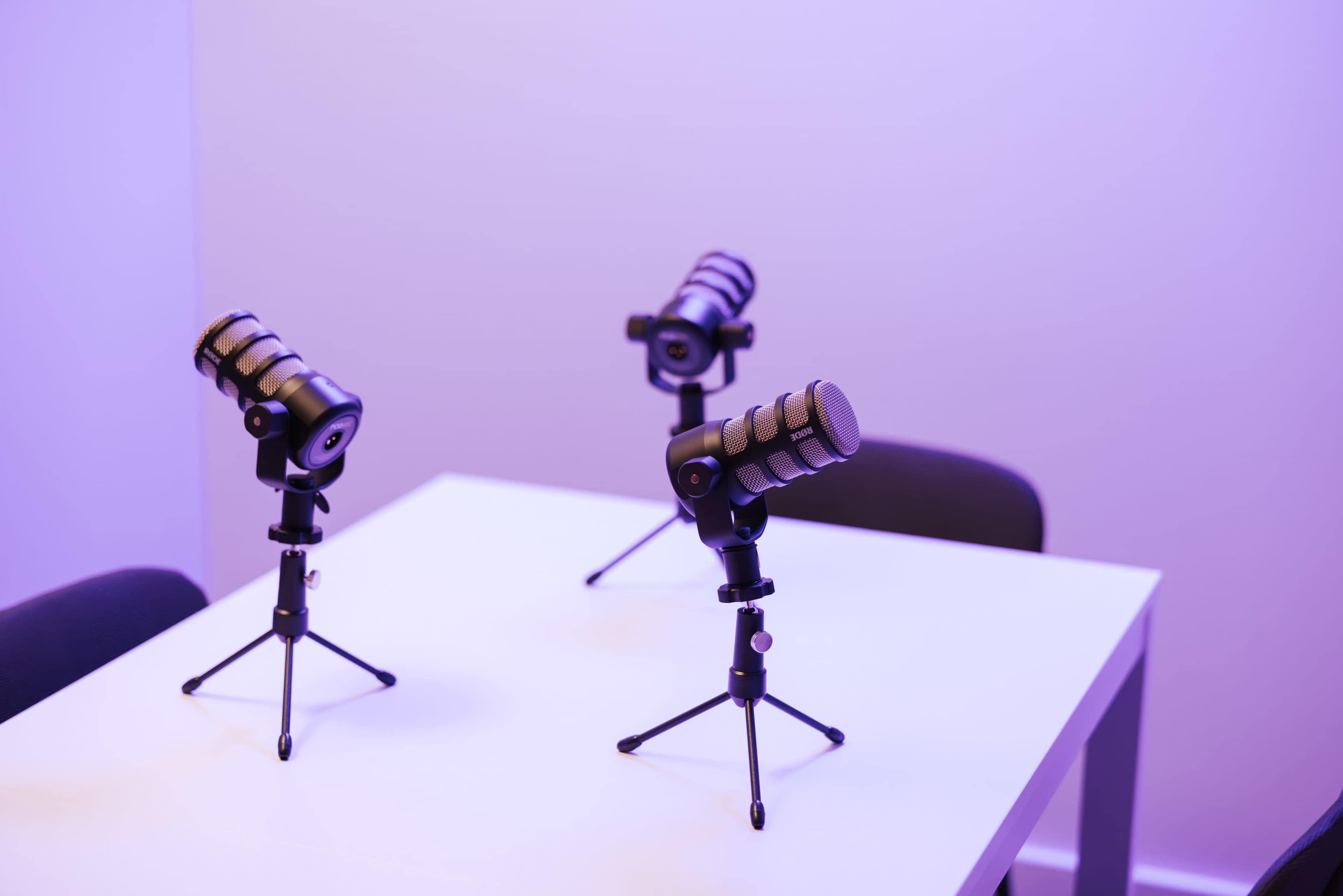 Three microphones on tripod stands are arranged on a white table in a softly lit purple room.