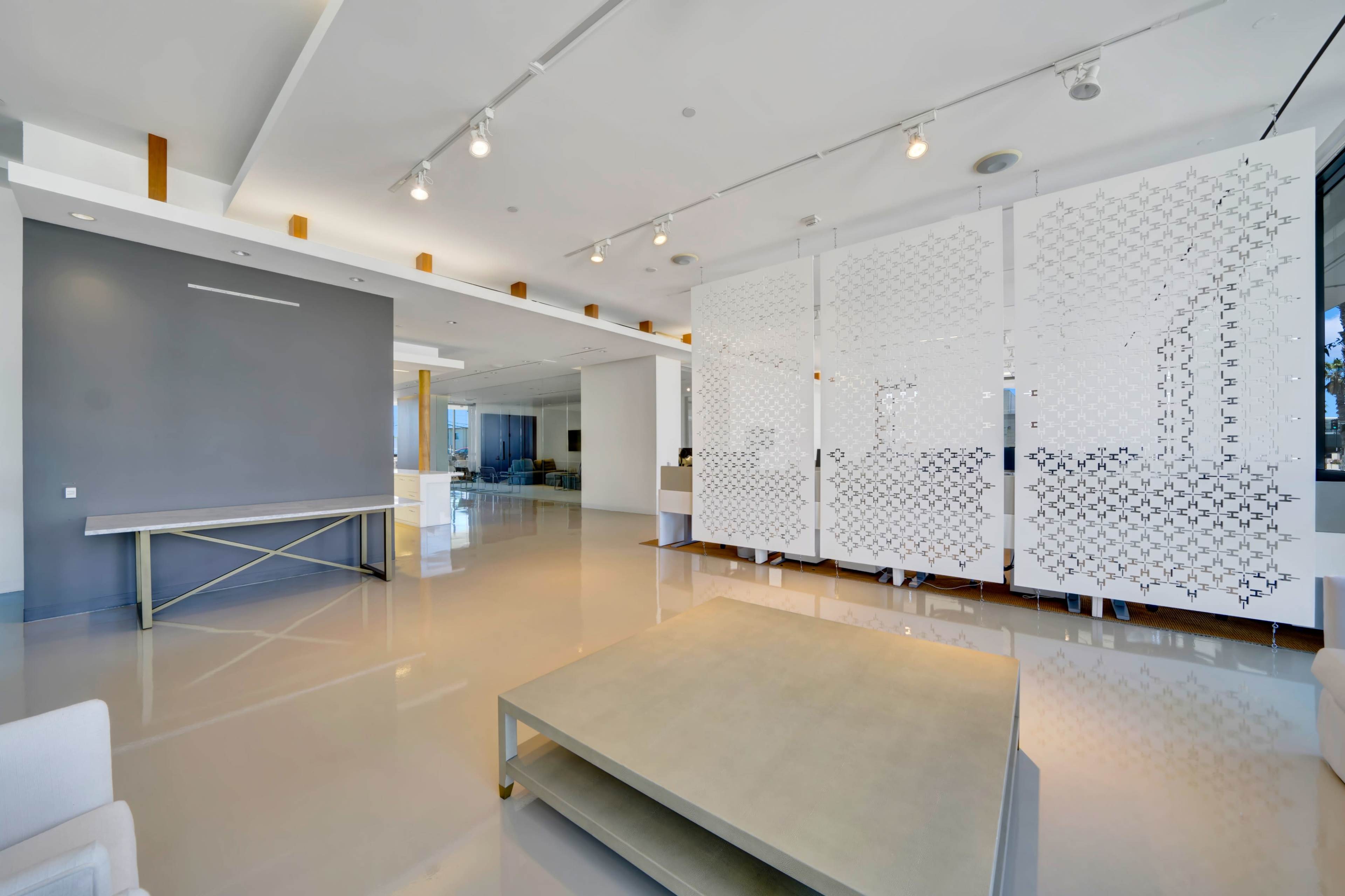 A modern, minimalist interior space with a light-colored floor, a large coffee table in the center, and a decorative partition dividing the area.