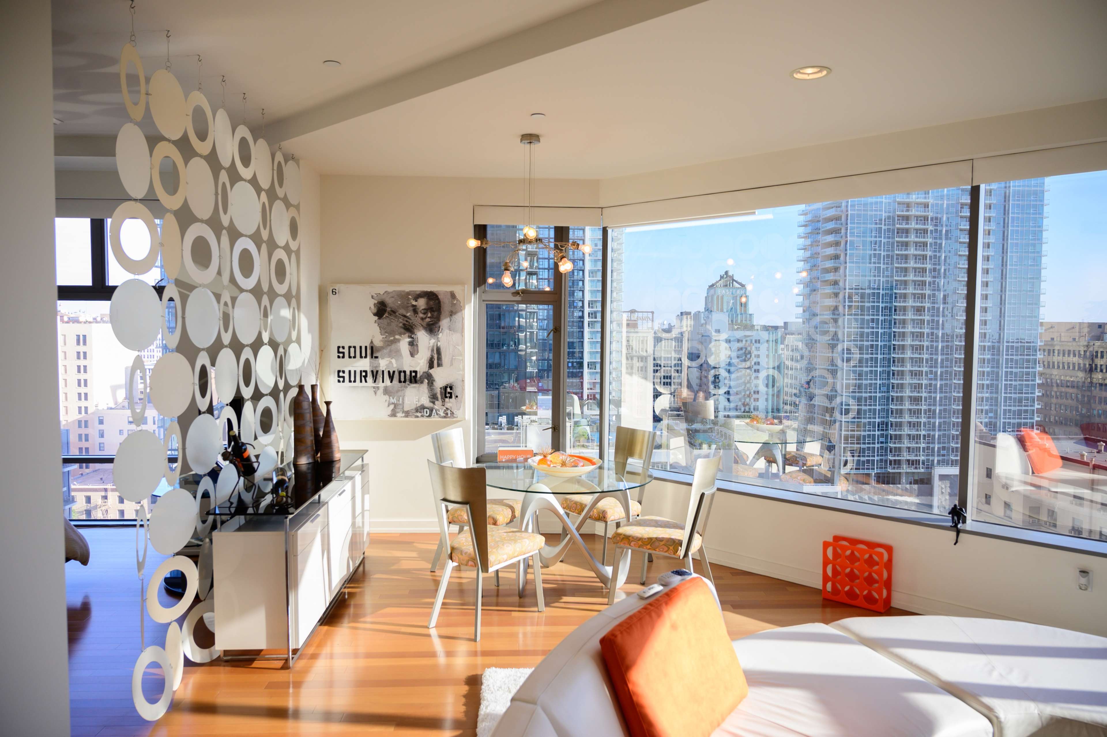 A modern apartment features a dining area with a circular partition and large windows overlooking a city skyline.